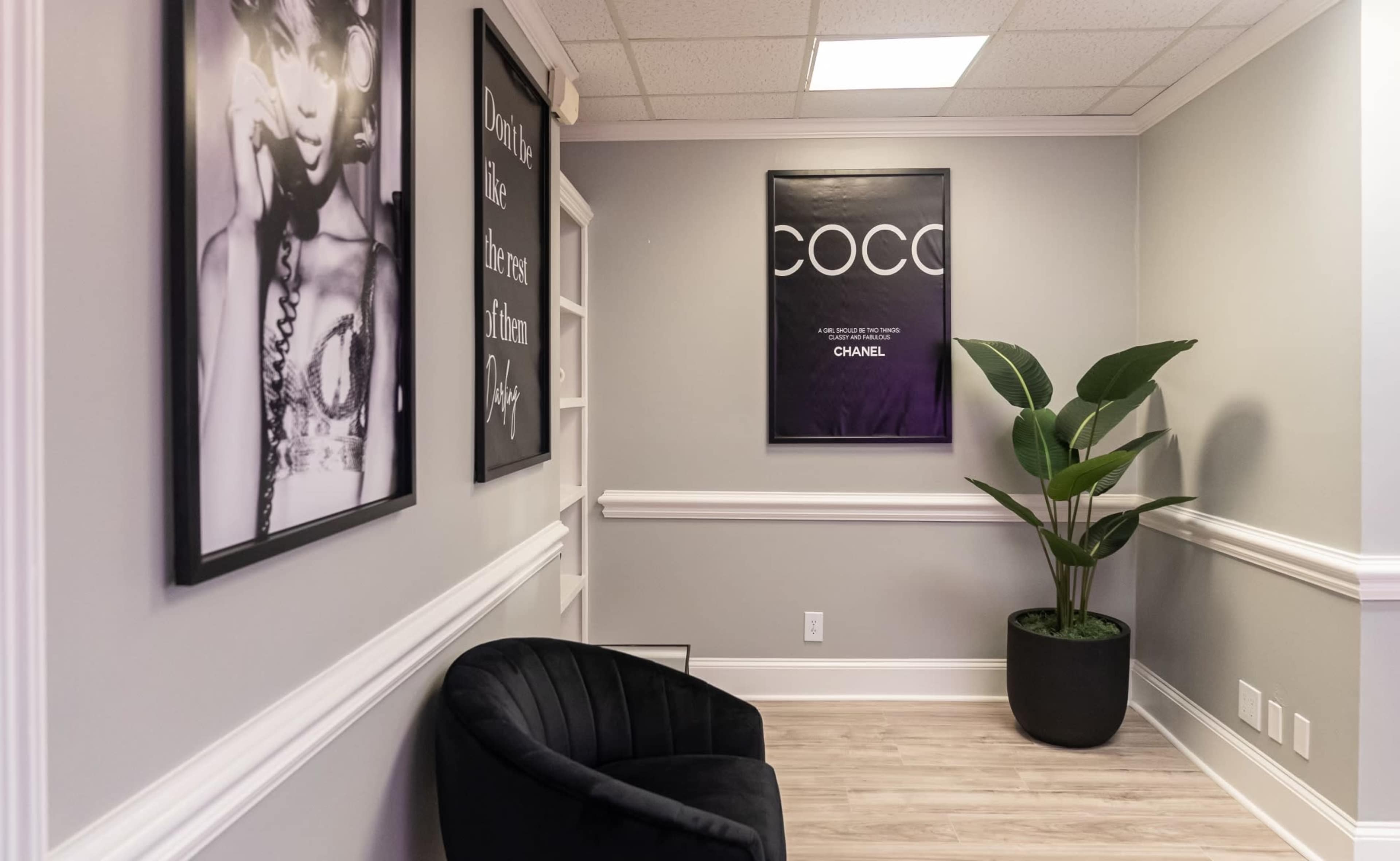 A stylish interior corner featuring a black armchair, a large potted plant, and framed artwork on the walls.