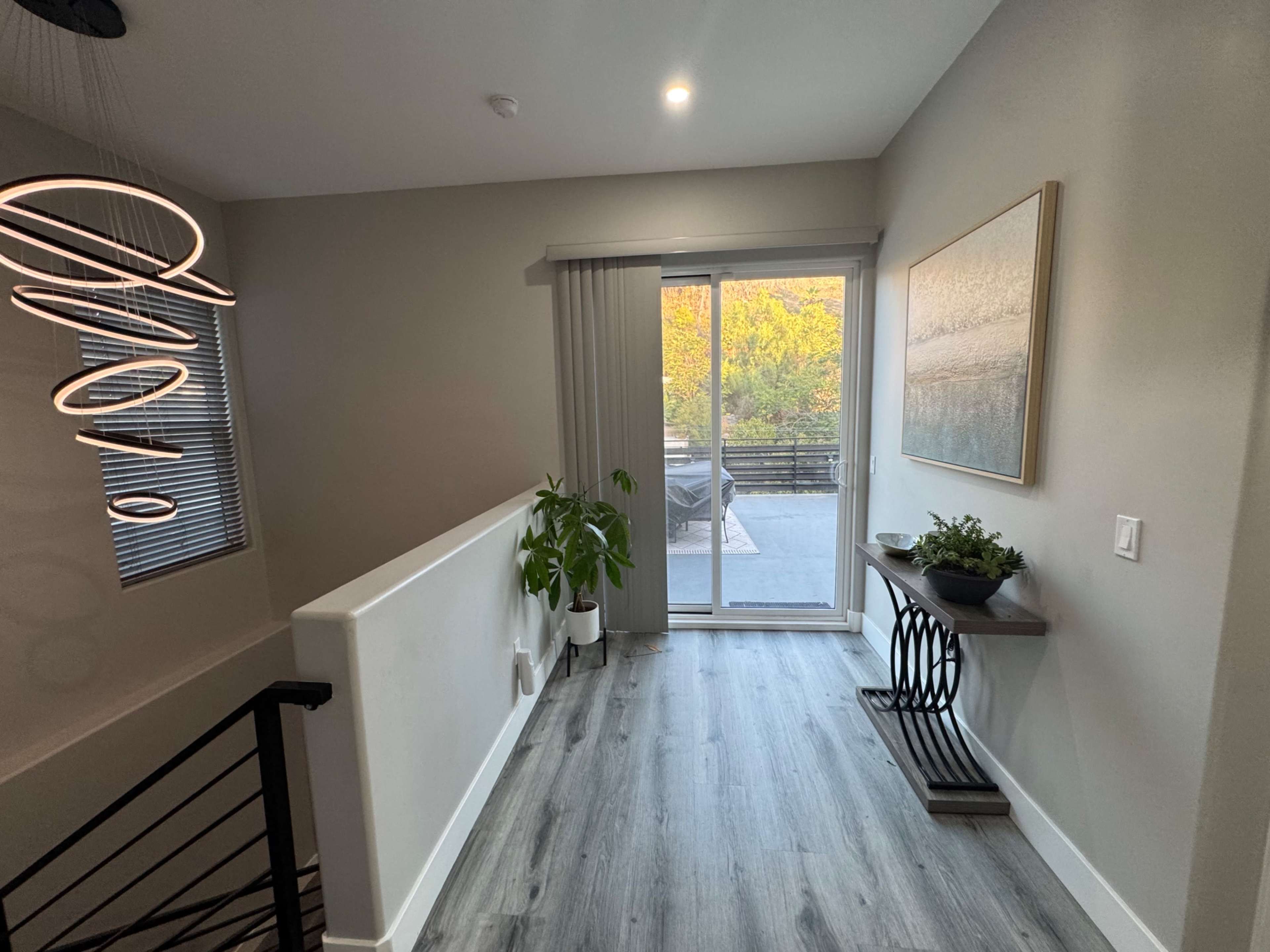 A well-lit hallway features a modern light fixture, a potted plant, and a sliding glass door leading to an outdoor space.