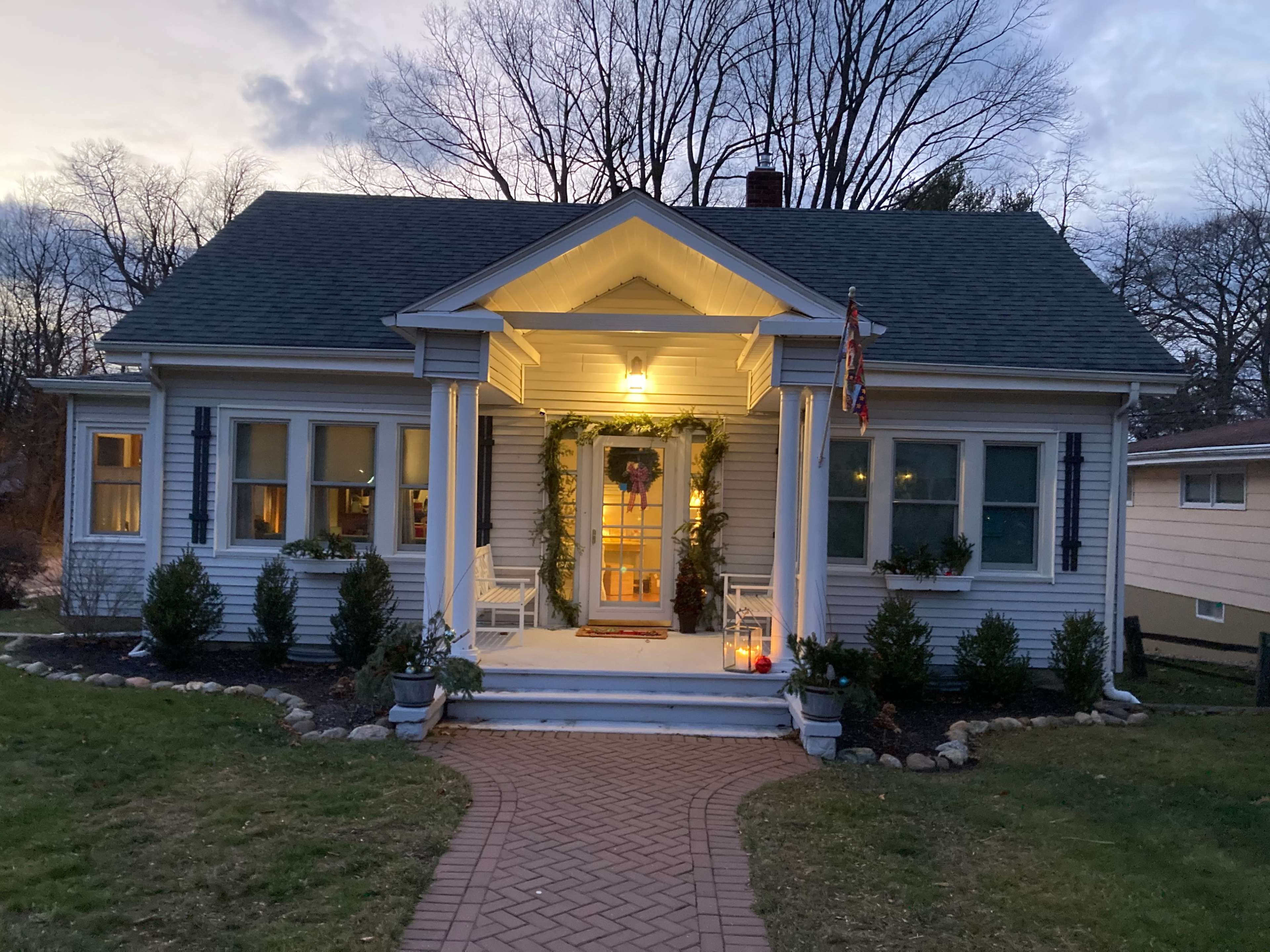 A well-lit, decorative house features a welcoming front porch adorned with plants and a pathway made of bricks leading to the entrance.