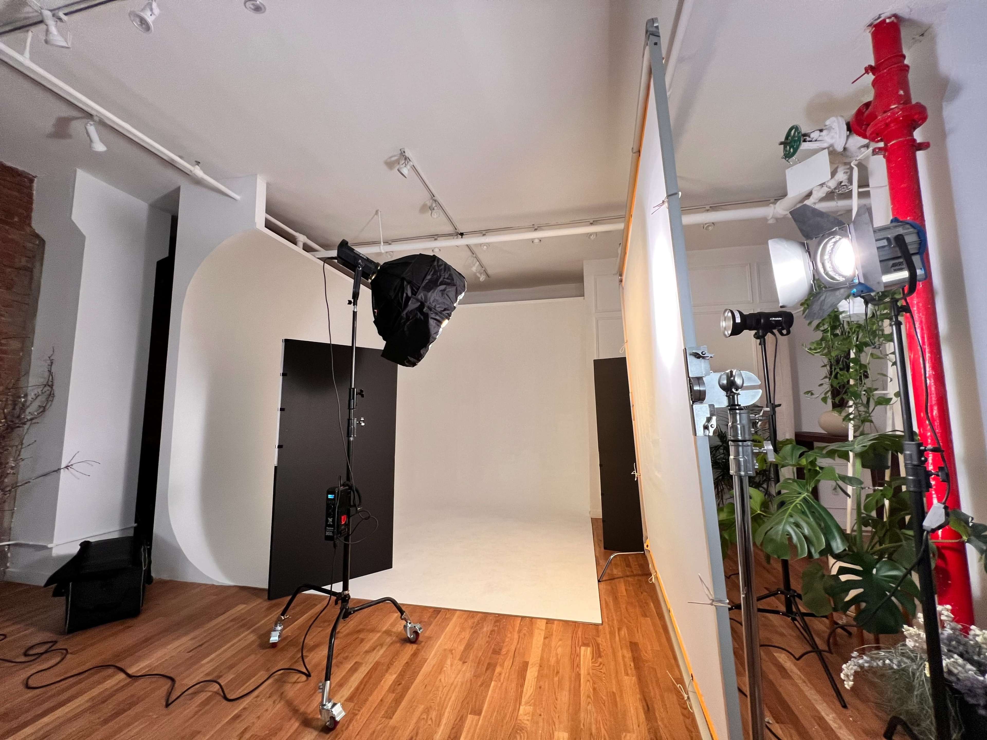 The image shows a photography studio setup featuring a curved backdrop, lighting equipment, and black panels arranged on a wooden floor.