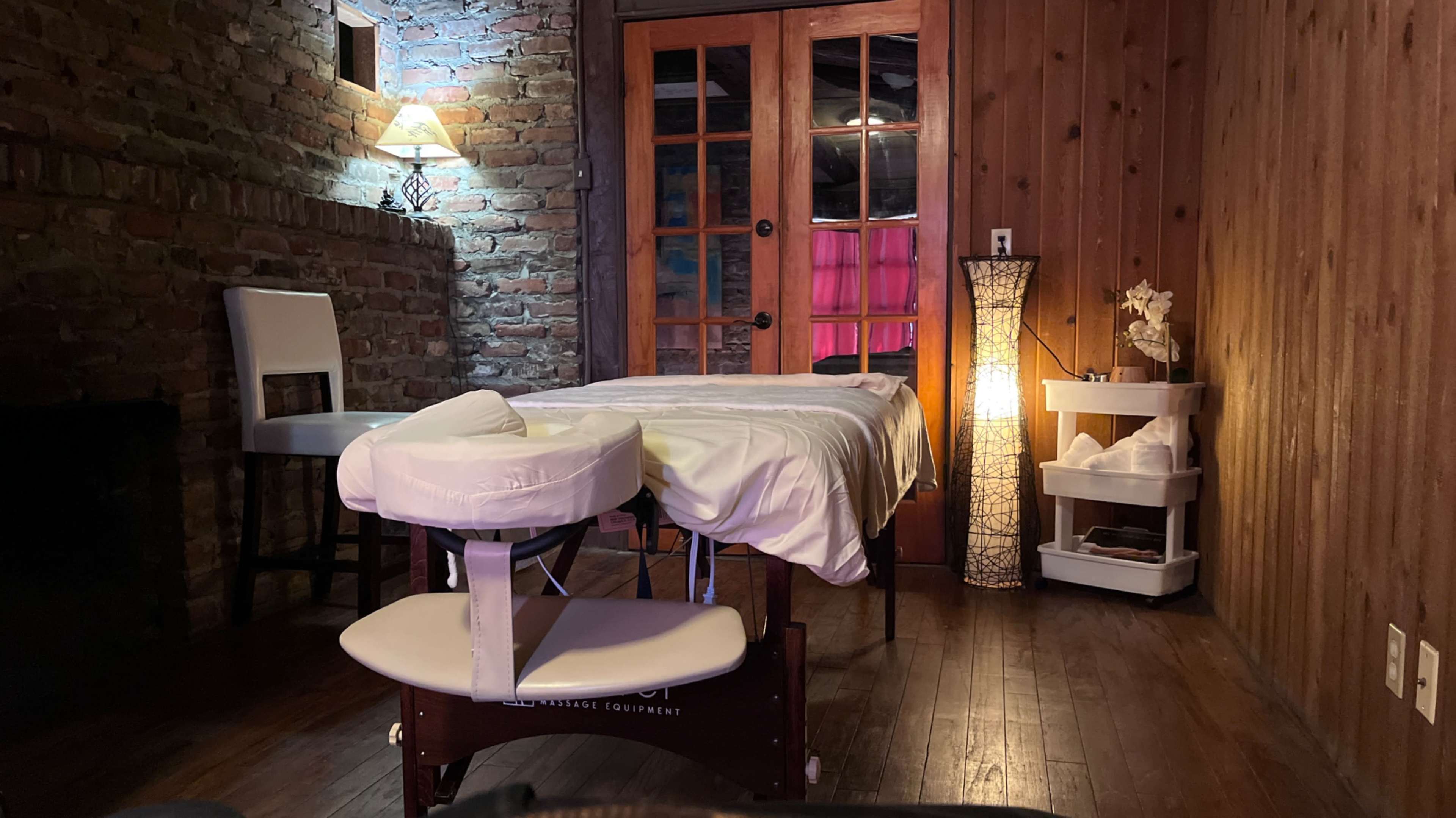 A massage therapy room features a massage table, a lamp, and wooden walls.
