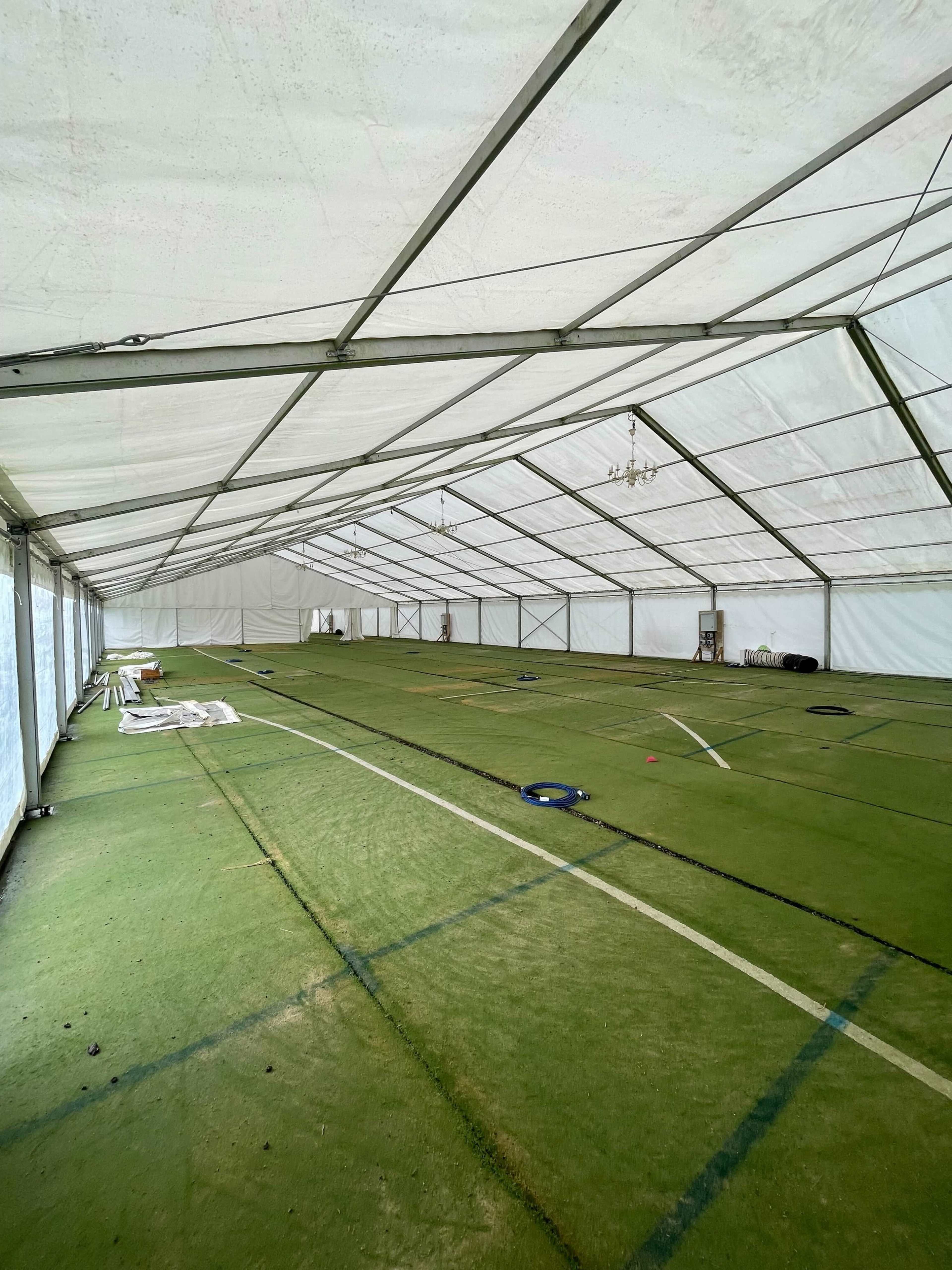 The image shows the interior of a large, empty tent with a green carpeted floor and clear sides, featuring unobstructed space and a few scattered items.