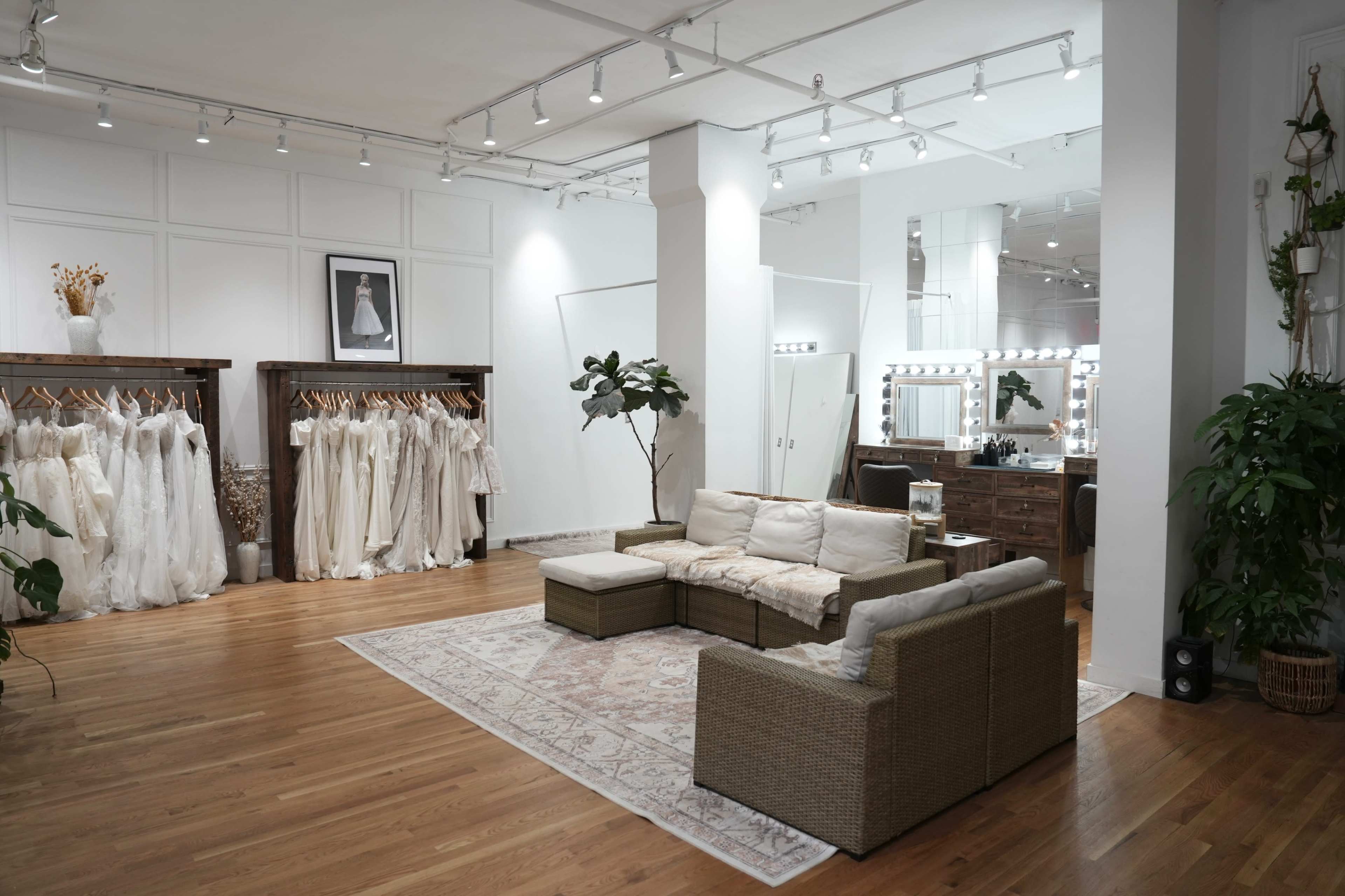 A bridal boutique features hanging wedding dresses, a cozy seating area, and a mirror-lit vanity station.