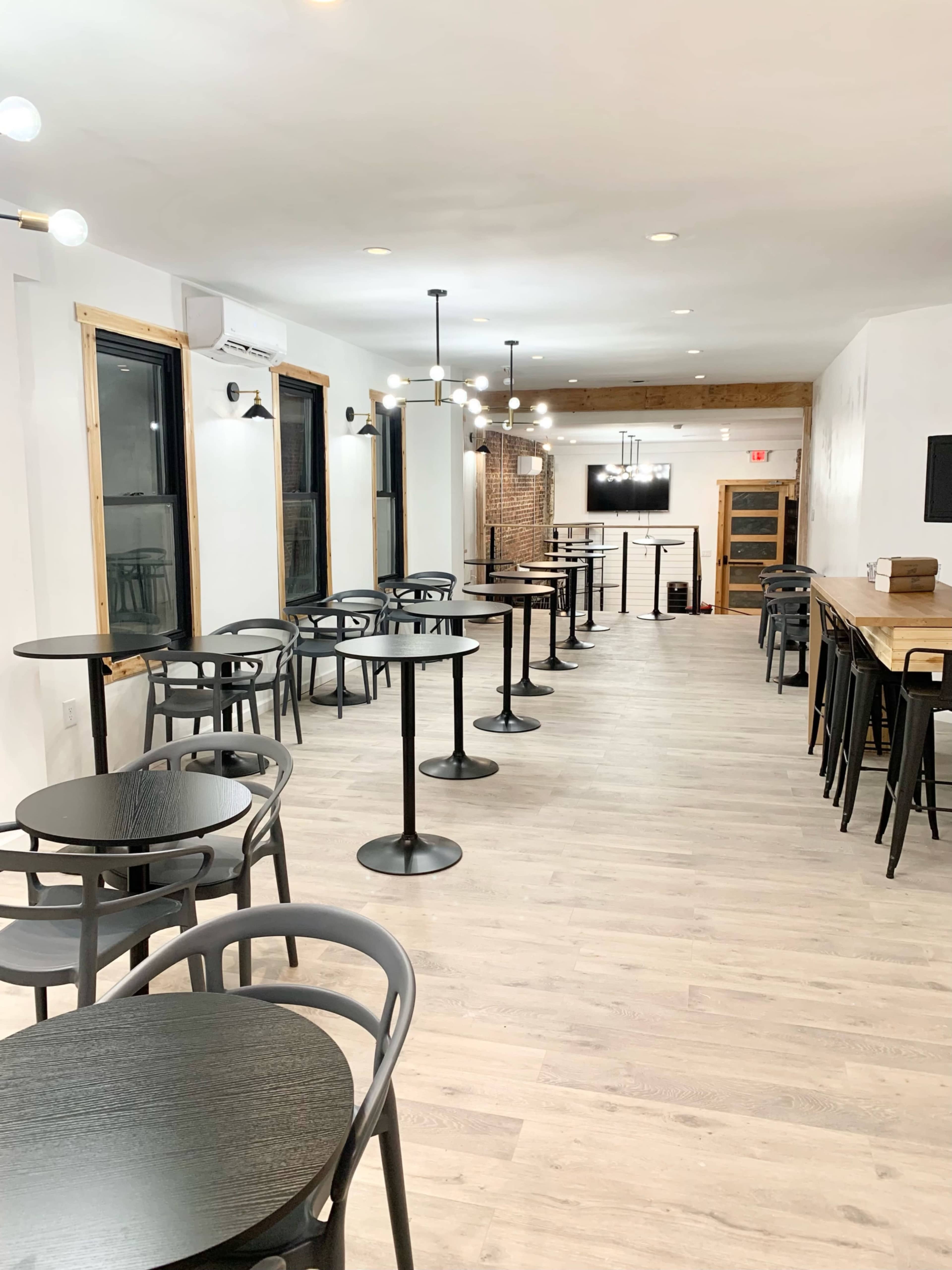 An empty café interior with several round tables and chairs arranged along the walls, and a long wooden counter at the end of the room.