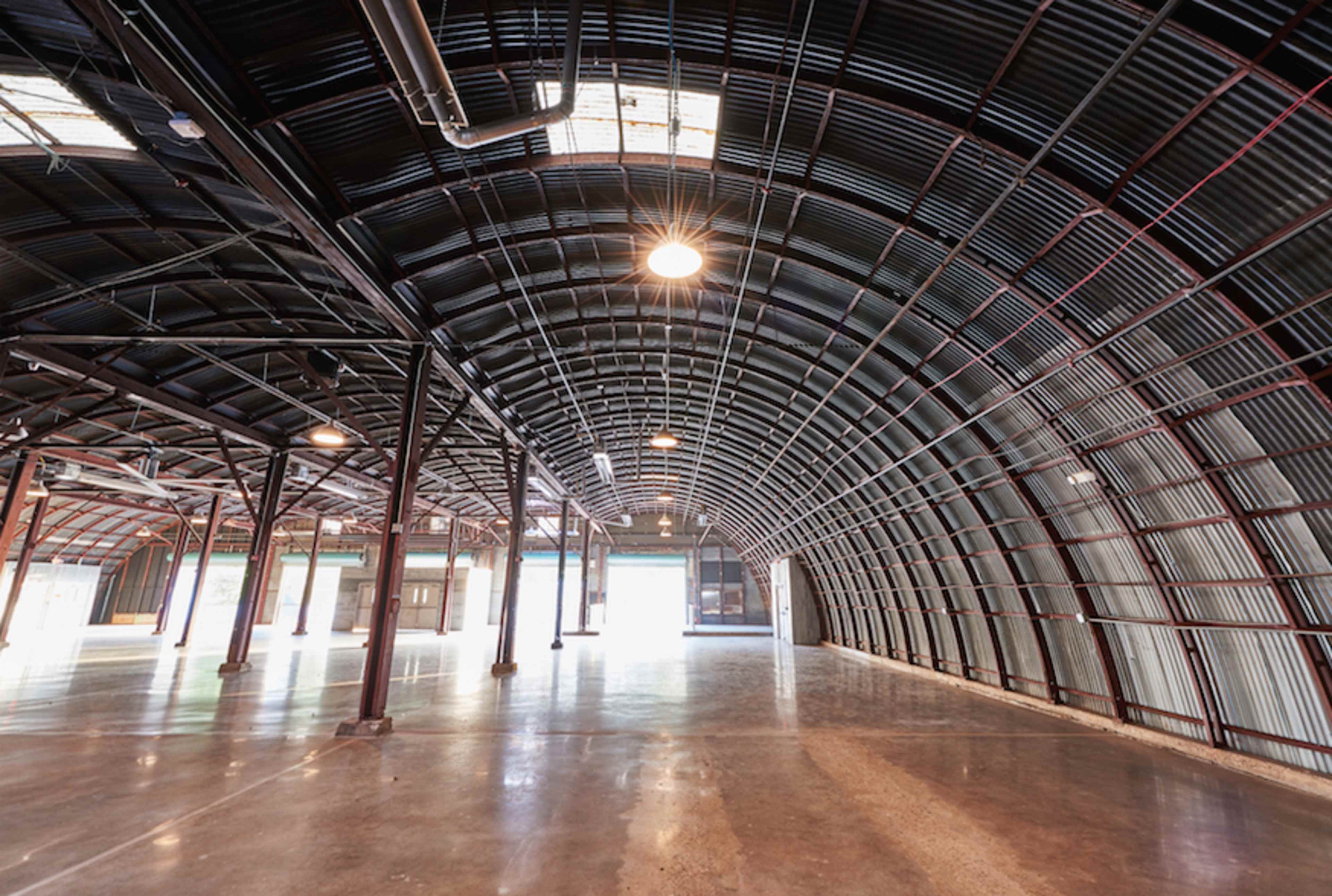 A large, empty industrial space with a curved metal roof and polished concrete floors.