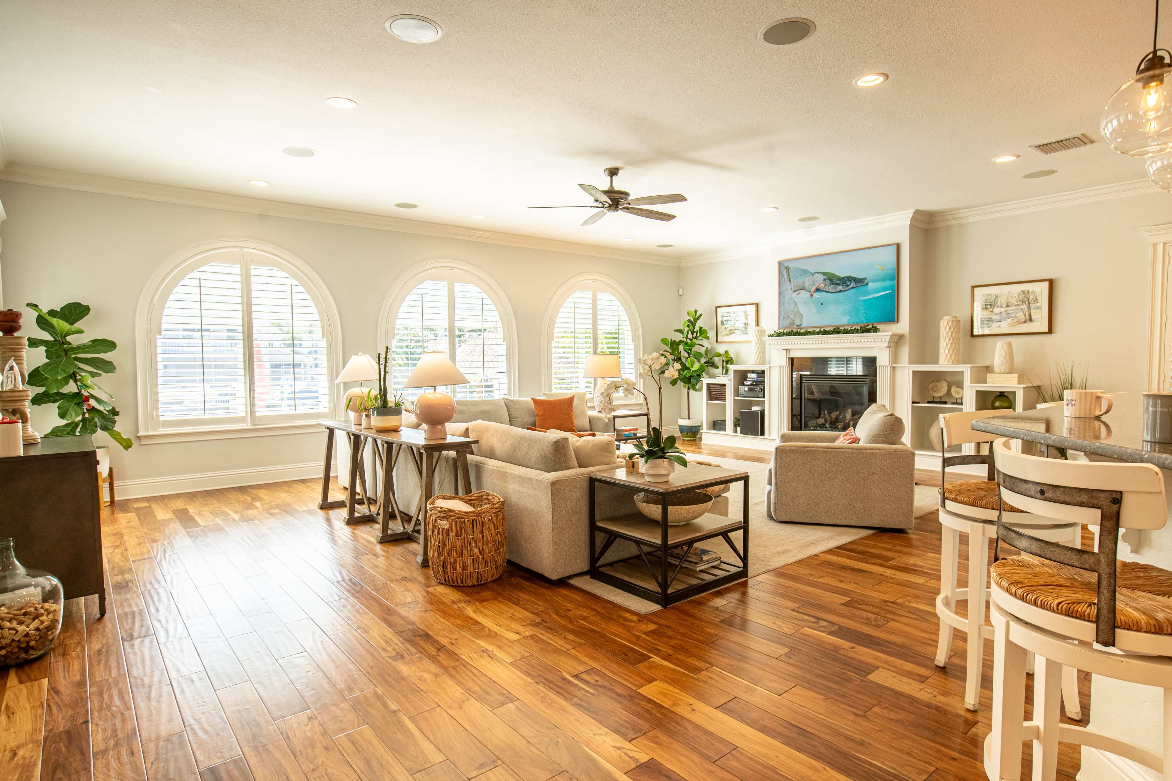 The spacious living room features large arched windows, a cozy seating area, and a fireplace, all illuminated by natural light.