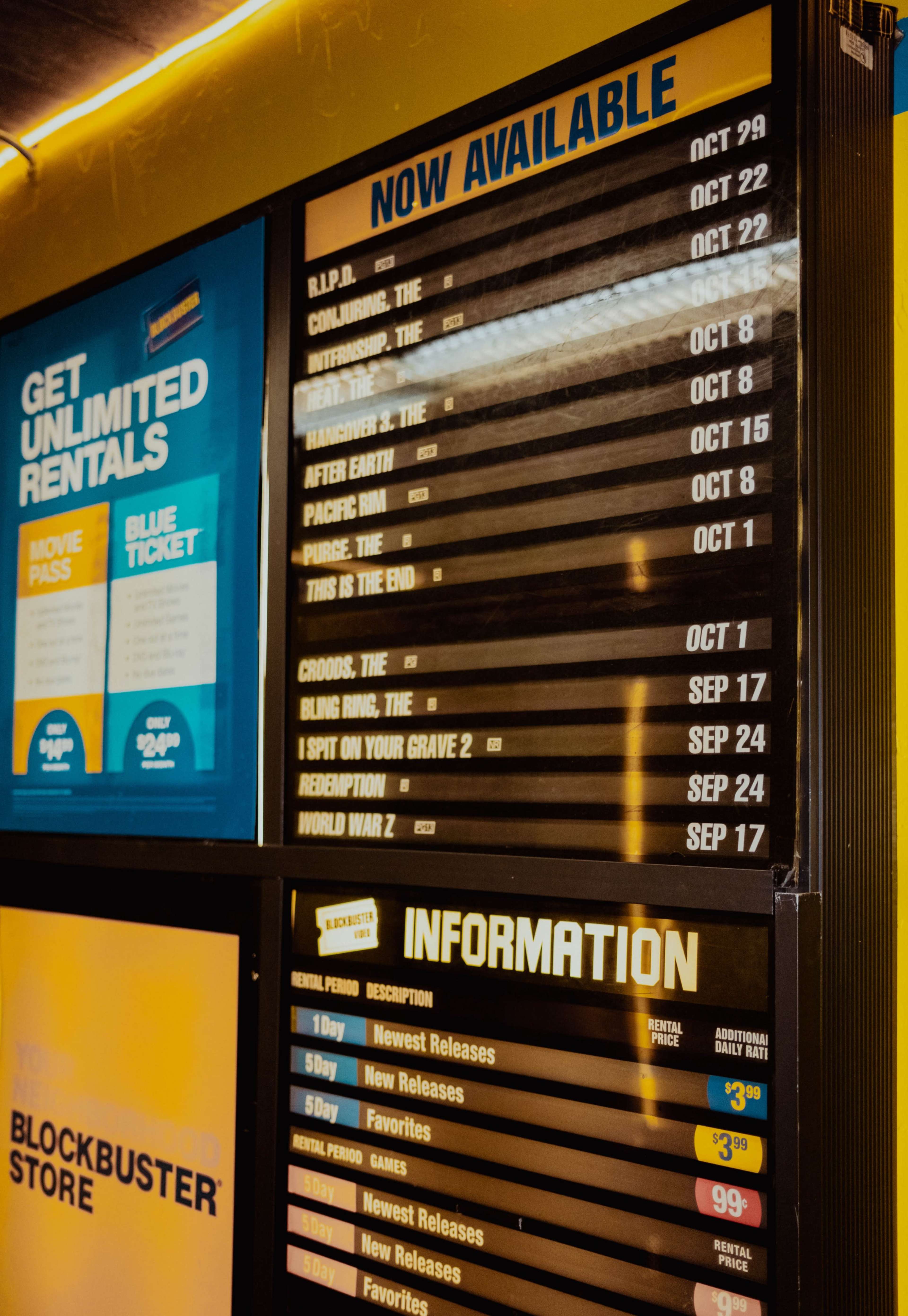 The image shows a display board with a list of movie titles, availability dates, and rental information for a Blockbuster store.