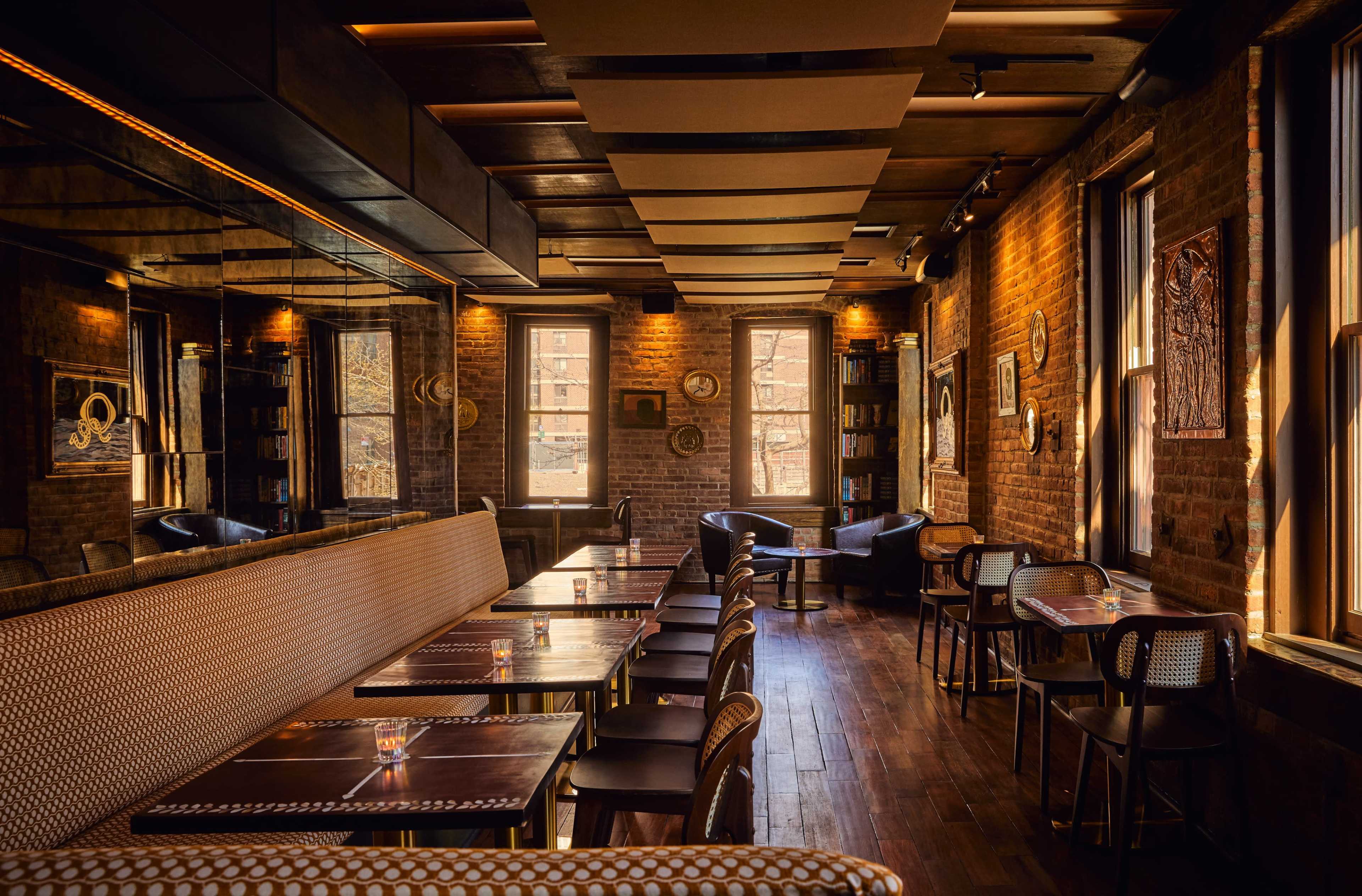The image shows a warmly lit restaurant with a mixture of tables and chairs, brick walls, and a mirrored section reflecting the interior design.