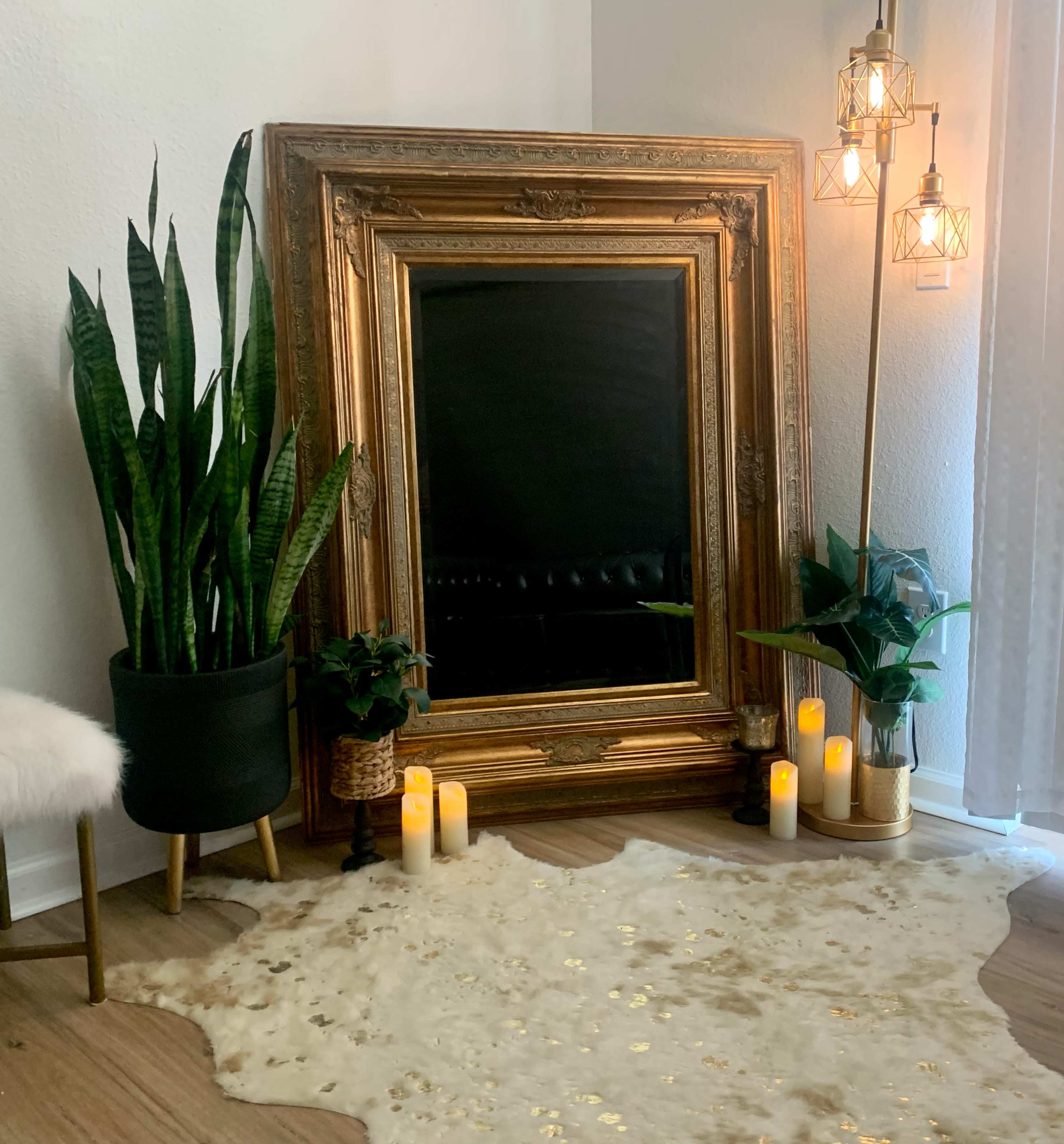 The scene features a large ornate golden mirror surrounded by plants, candles, and a decorative rug on a wooden floor.