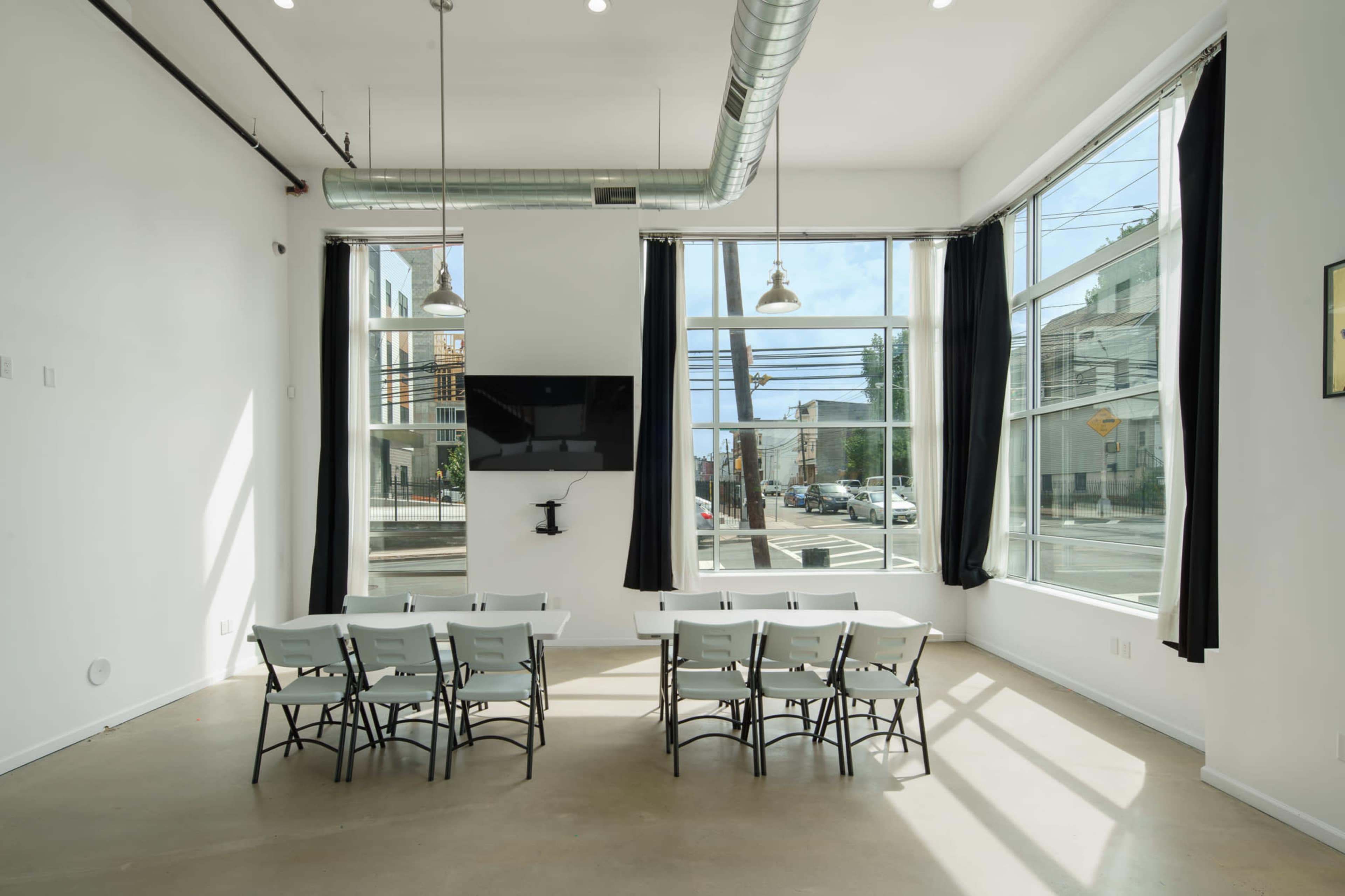 A bright and airy meeting room features a row of chairs facing a wall-mounted screen, with large windows allowing natural light to fill the space.