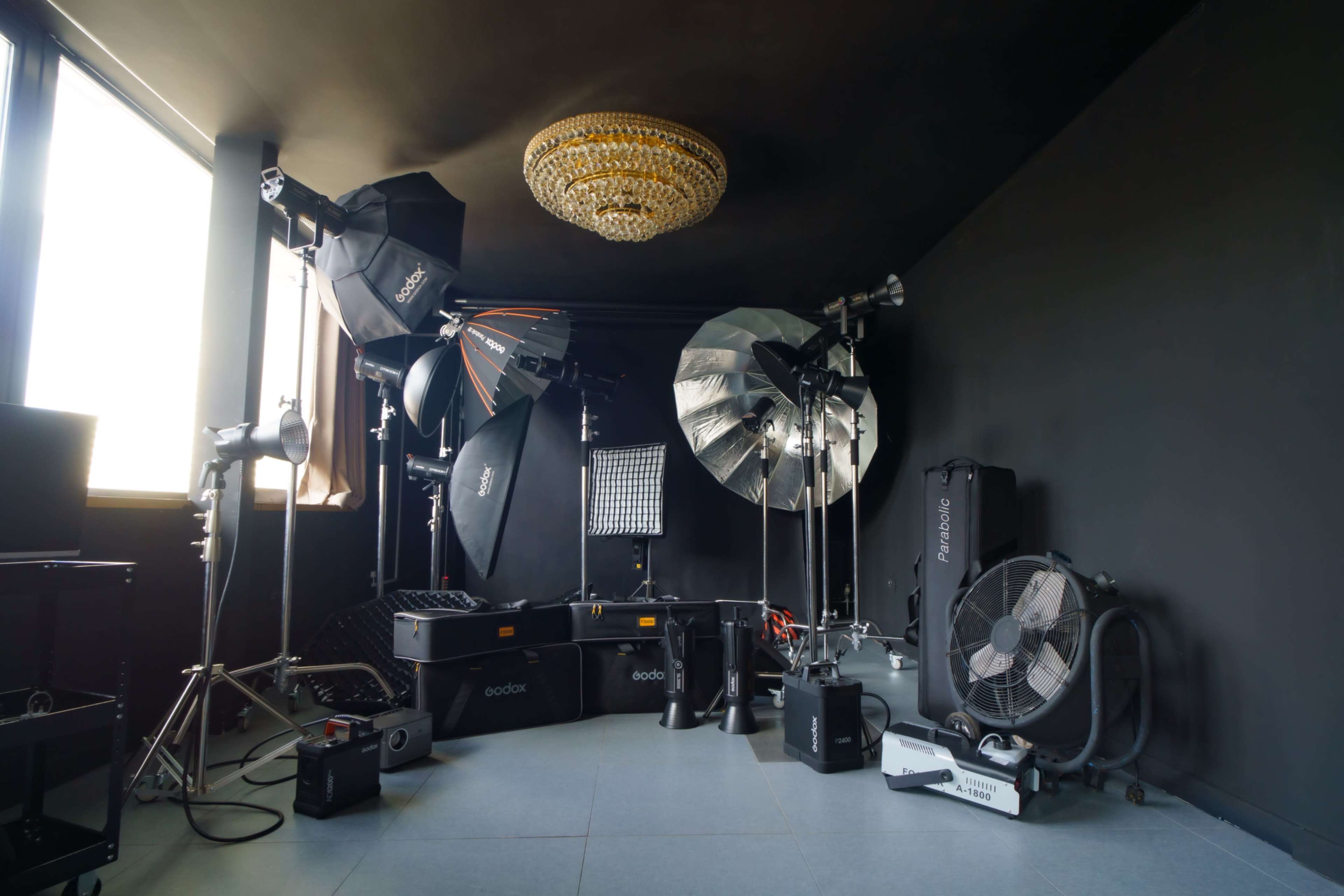 The image shows a photography studio equipped with various lighting setups, modifiers, and a large chandelier in the corner.