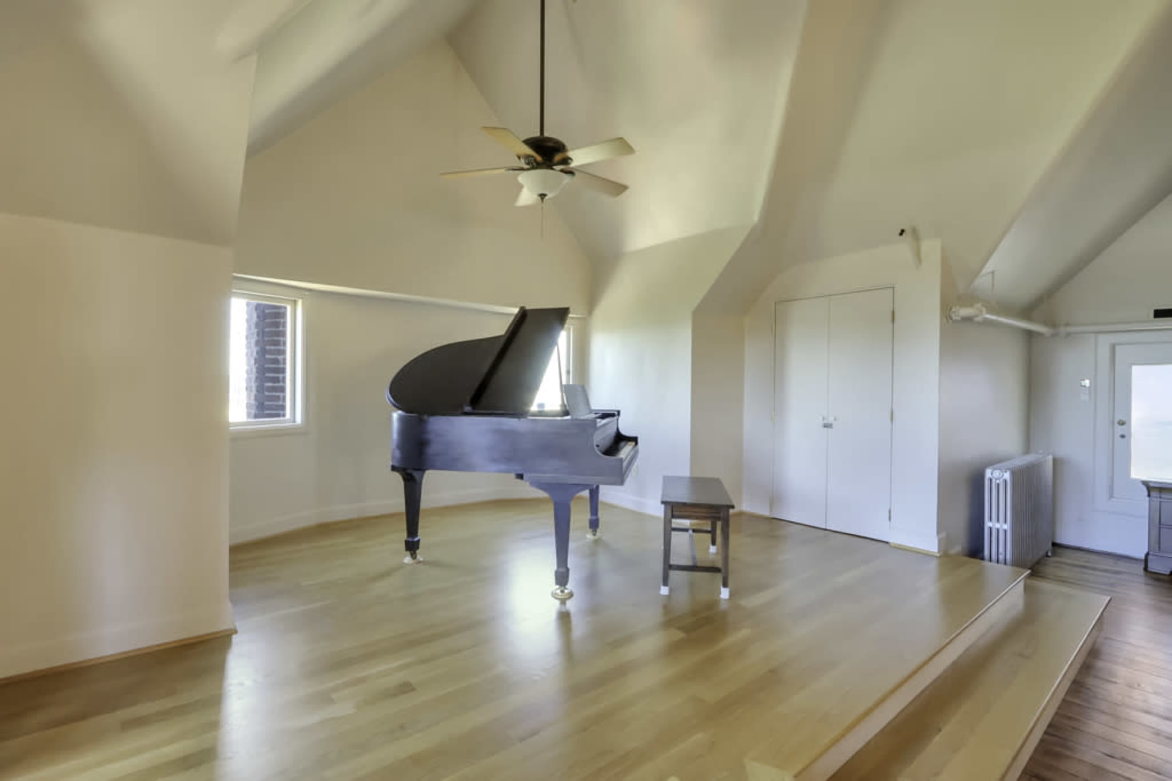 A spacious room with high ceilings featuring a grand piano, a small bench, and a window.