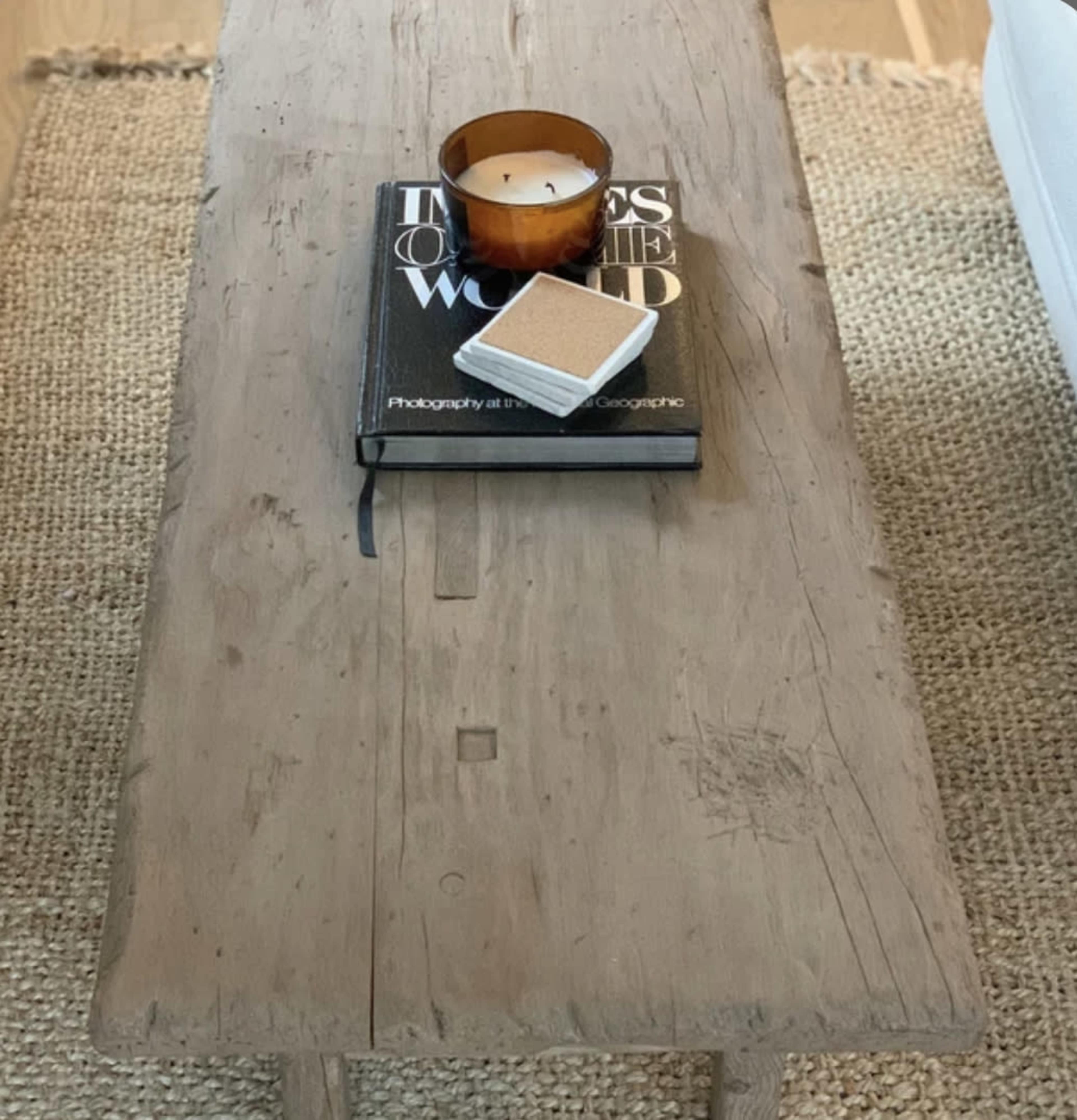 A wooden coffee table holds a book, a candle, and a small decorative item, positioned on a woven rug.
