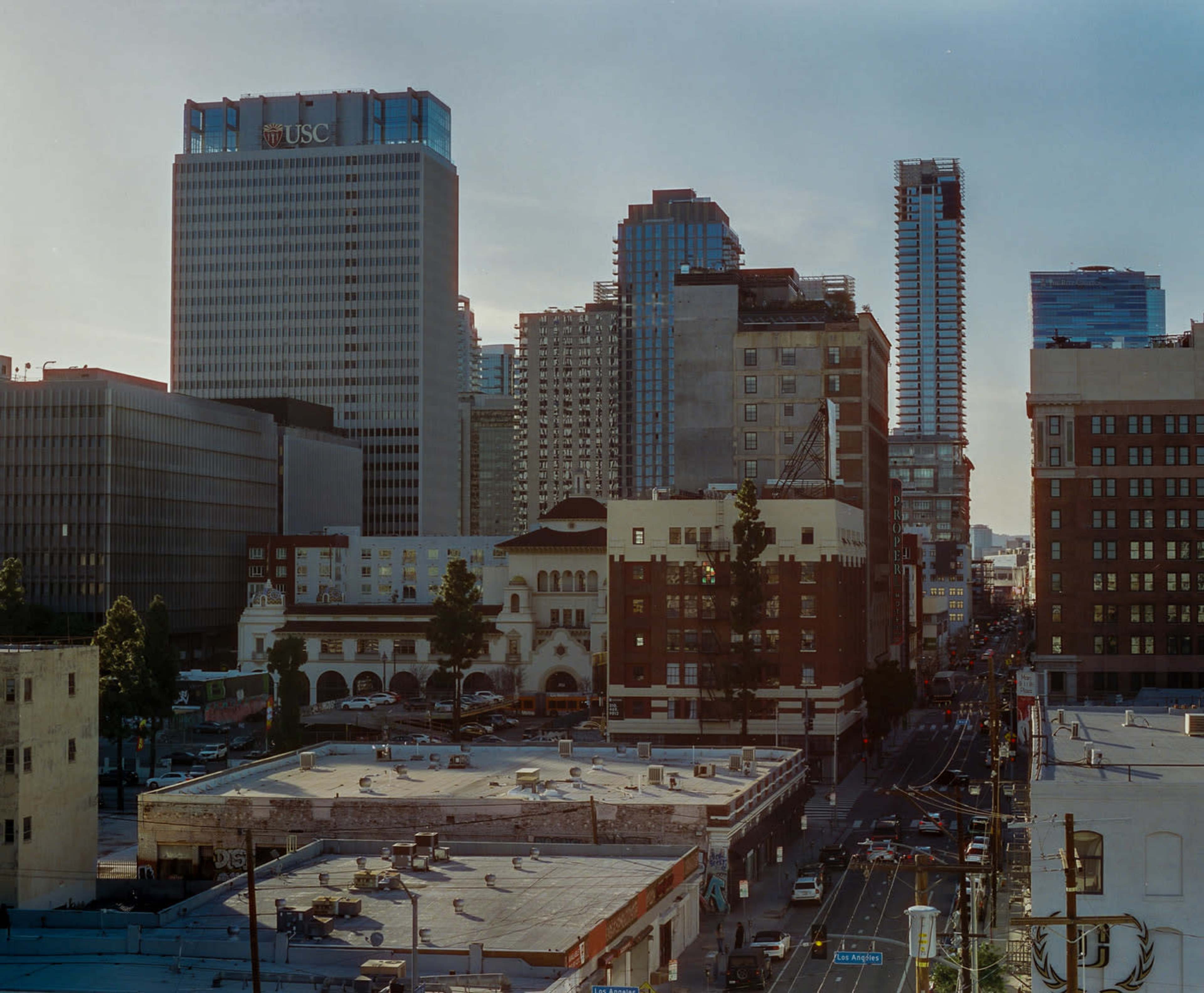 The image depicts a cityscape featuring a mix of modern skyscrapers and historic buildings, with a view of a bustling street lined with vehicles.