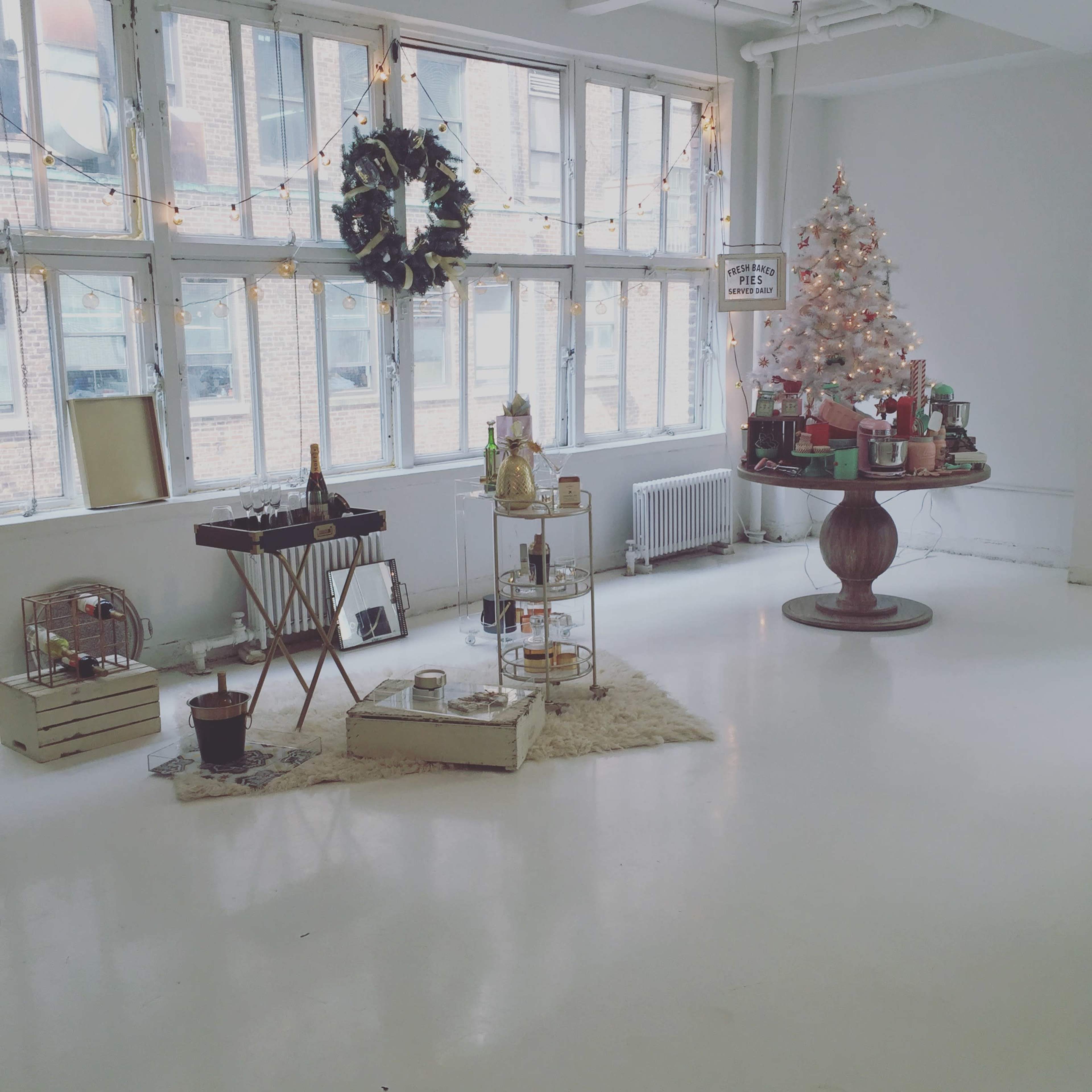 A bright, minimalist interior with large windows, a decorated Christmas tree on one side, and a festive setup including a bar cart on the other side.
