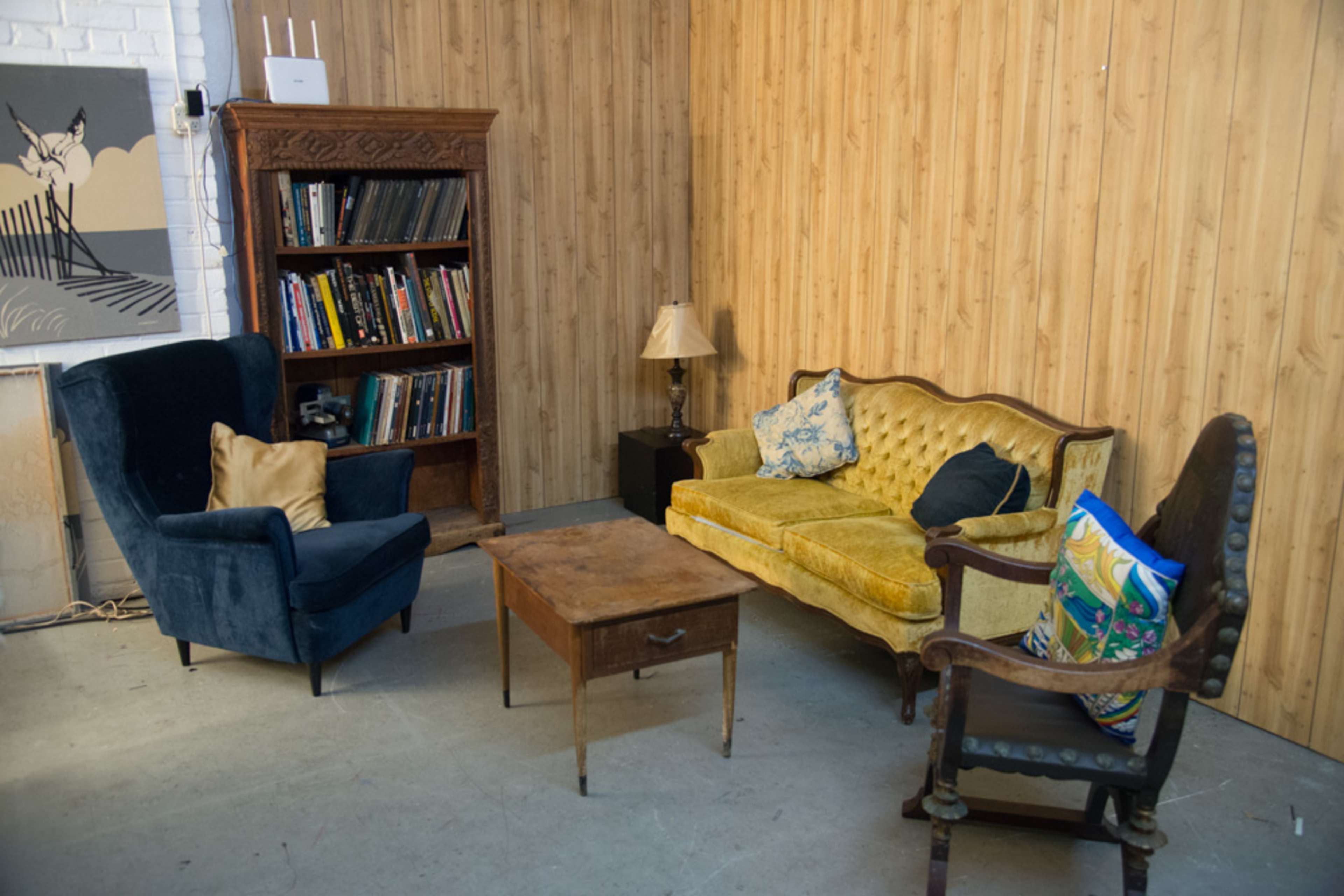 A small living area with two upholstered chairs, a yellow sofa, a wooden coffee table, and a bookcase against a wooden-paneled wall.