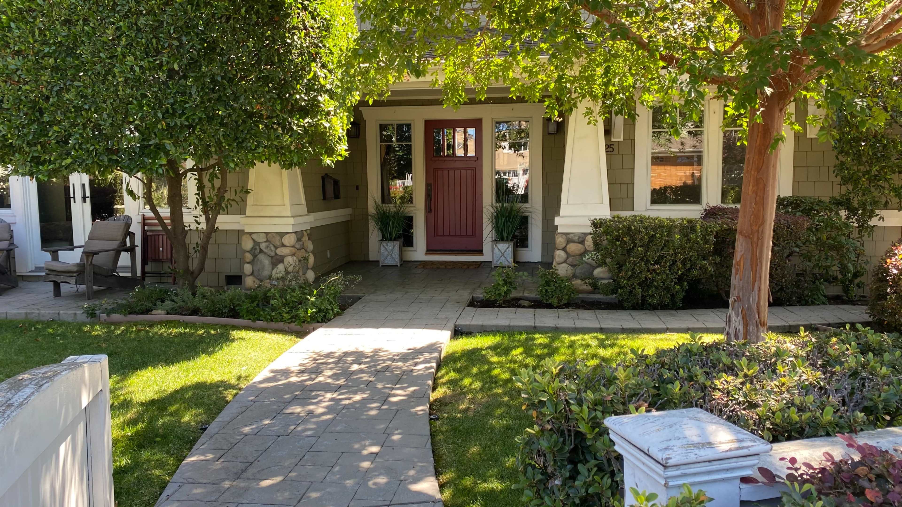 A stone pathway leads to a house with a red front door, framed by trees and landscaped greenery.