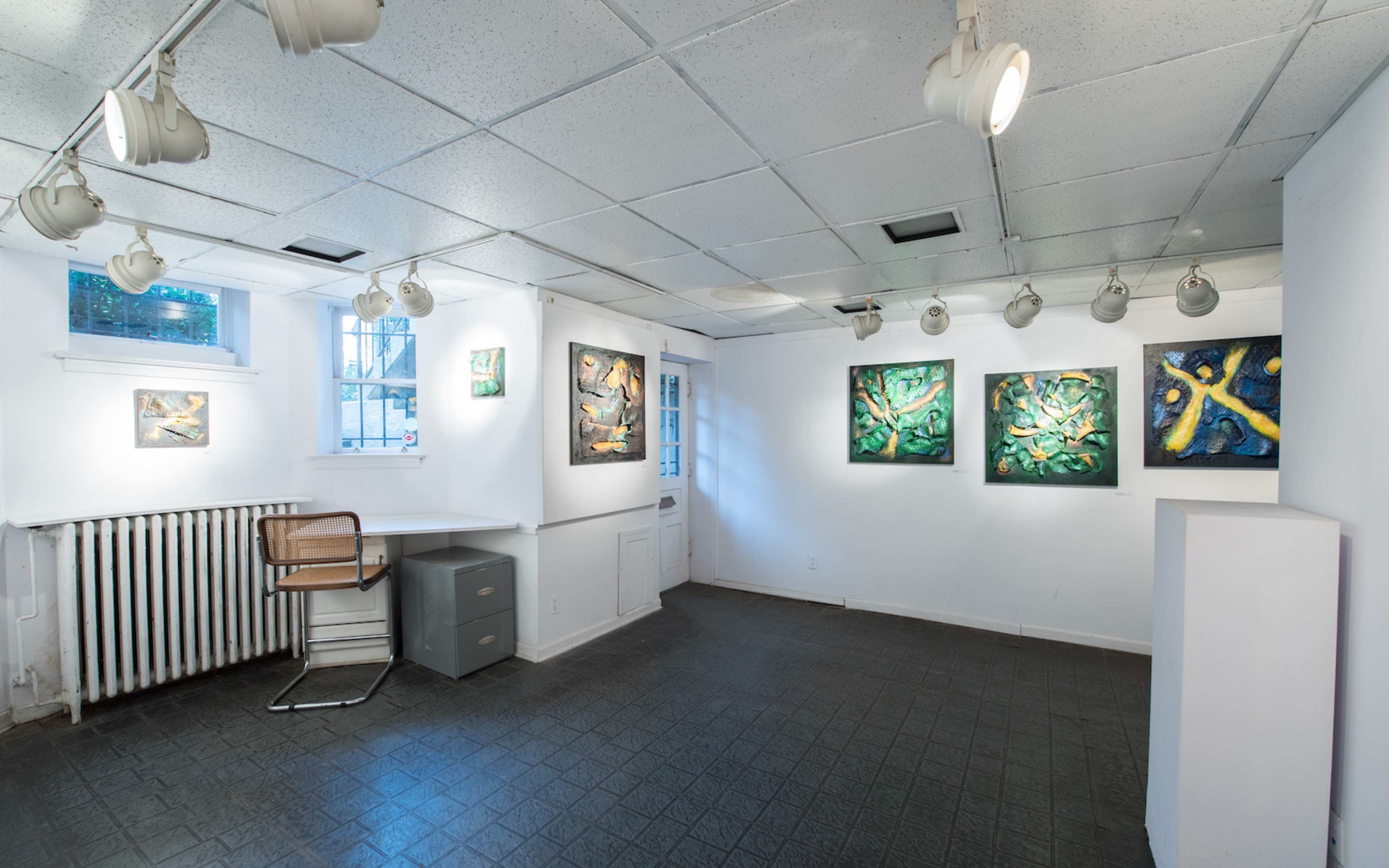 An art gallery featuring several colorful paintings on the walls and a desk with a chair in the corner.