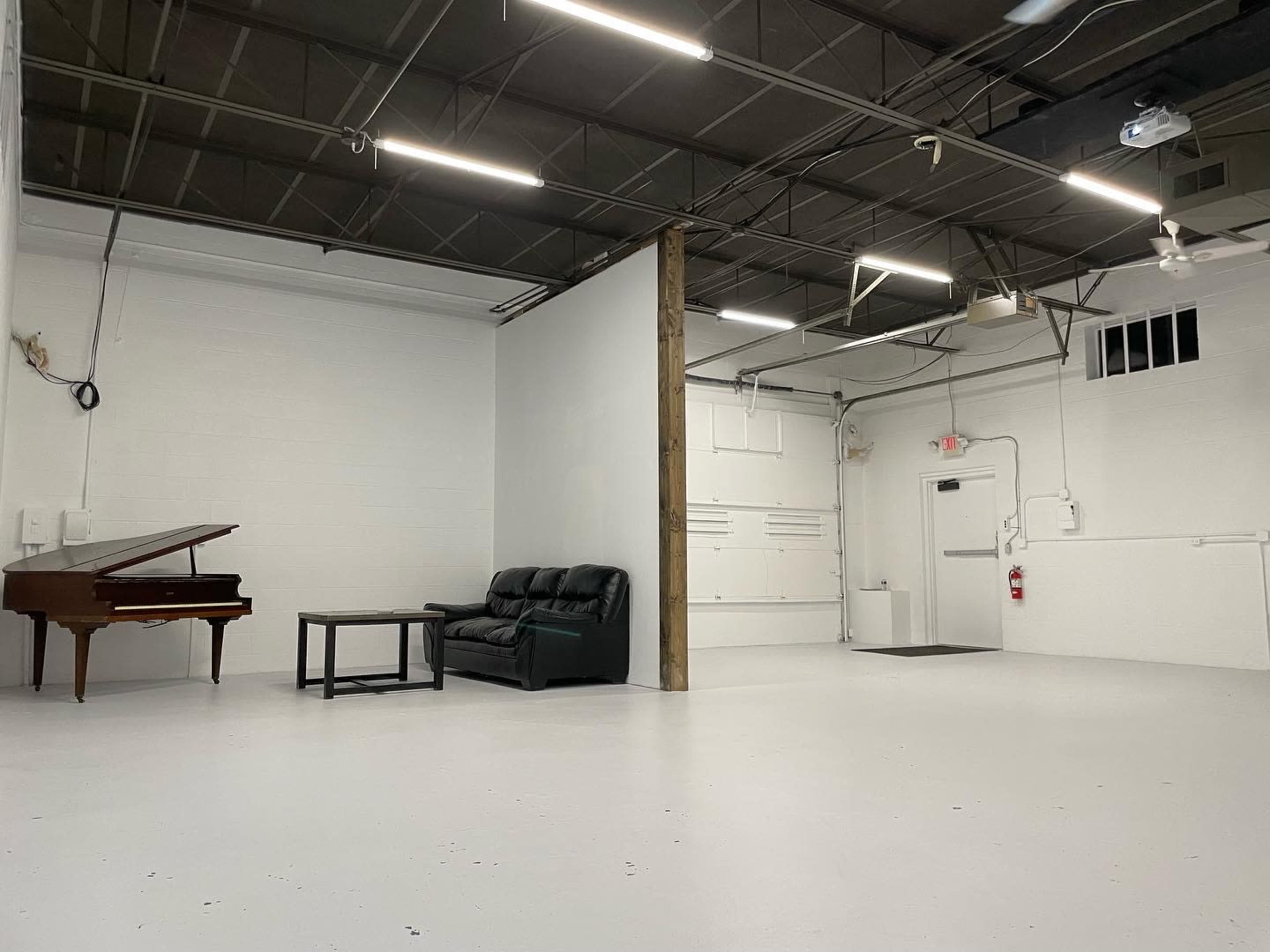 A spacious interior with a piano, a black loveseat, and a coffee table against a white wall.