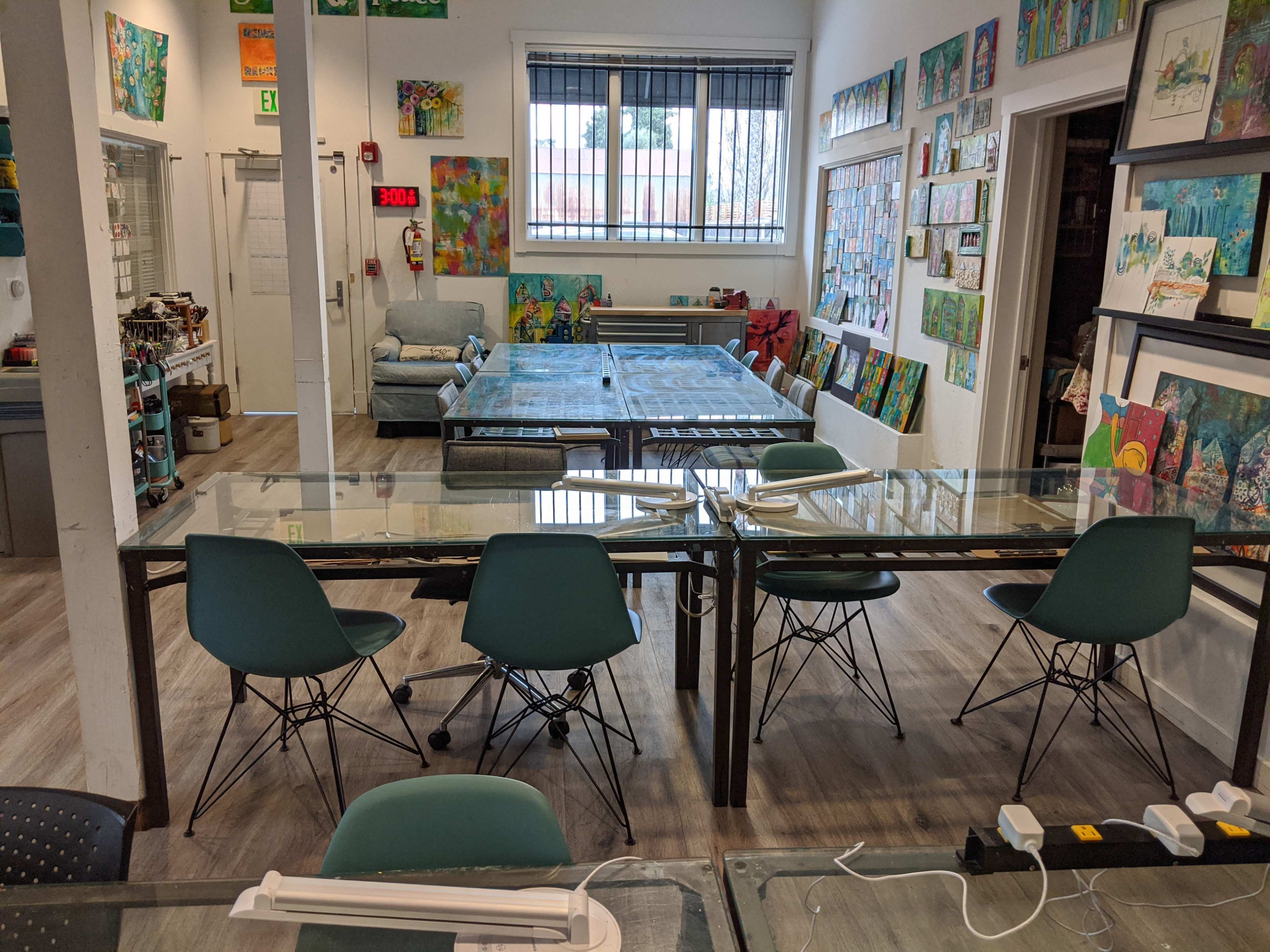 An art studio with several tables, chairs, and walls adorned with colorful paintings.