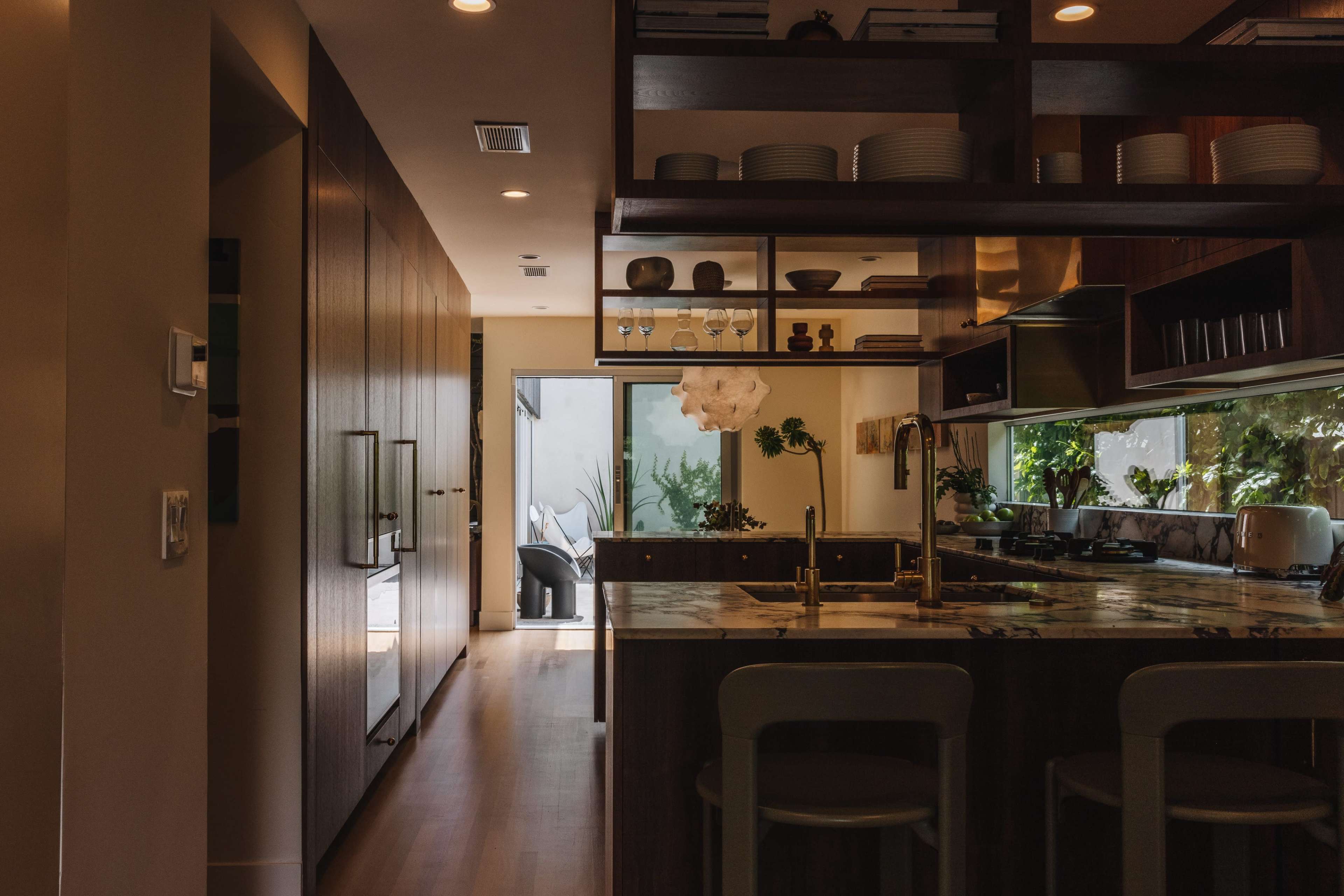 A modern kitchen features a marble countertop, wooden cabinetry, and a view of an outdoor patio through large glass doors.
