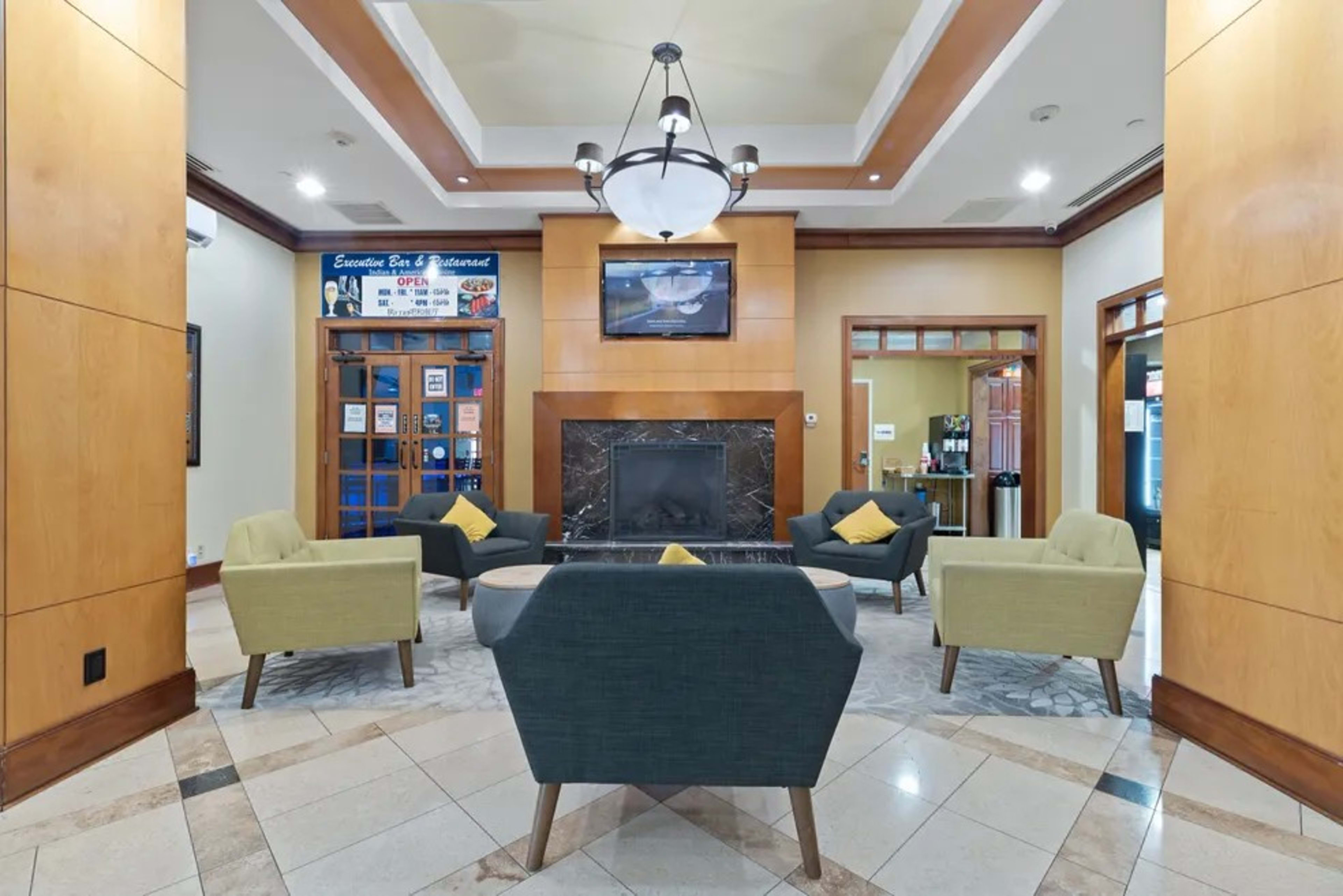 A hotel lobby featuring a seating area with four chairs and a coffee table arranged around a fireplace, with a television mounted above it.