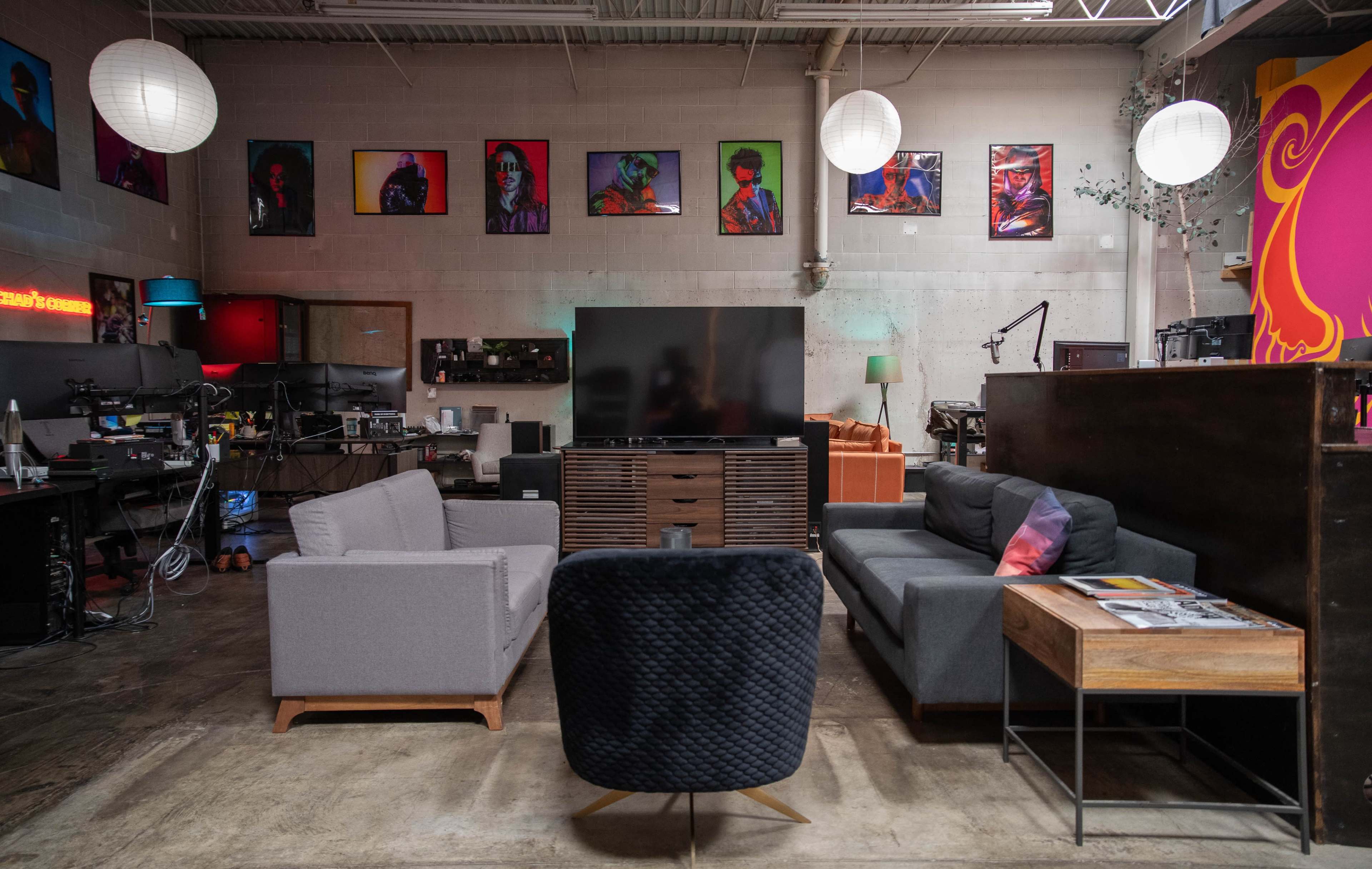 A modern living room area with two sofas, a coffee table, and a large TV, surrounded by colorful artwork on the walls.