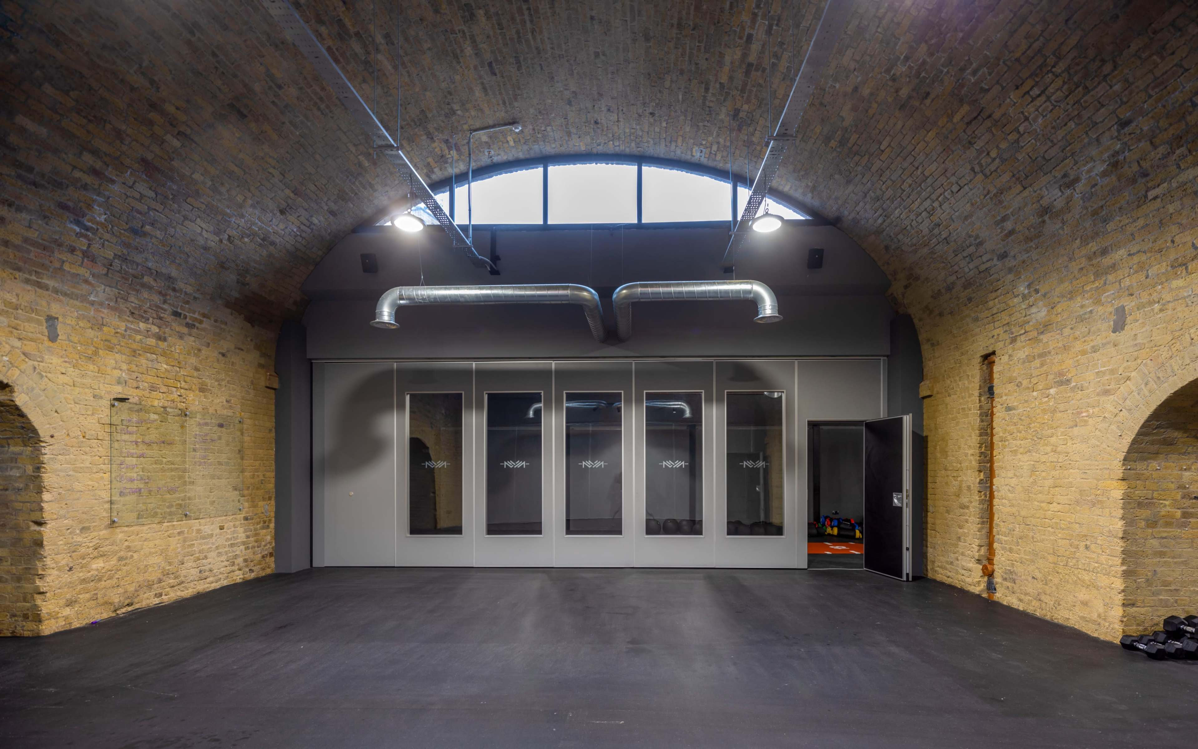 A spacious interior with exposed brick walls, high arched ceilings, and a section of transparent glass doors leading to an area with fitness equipment.