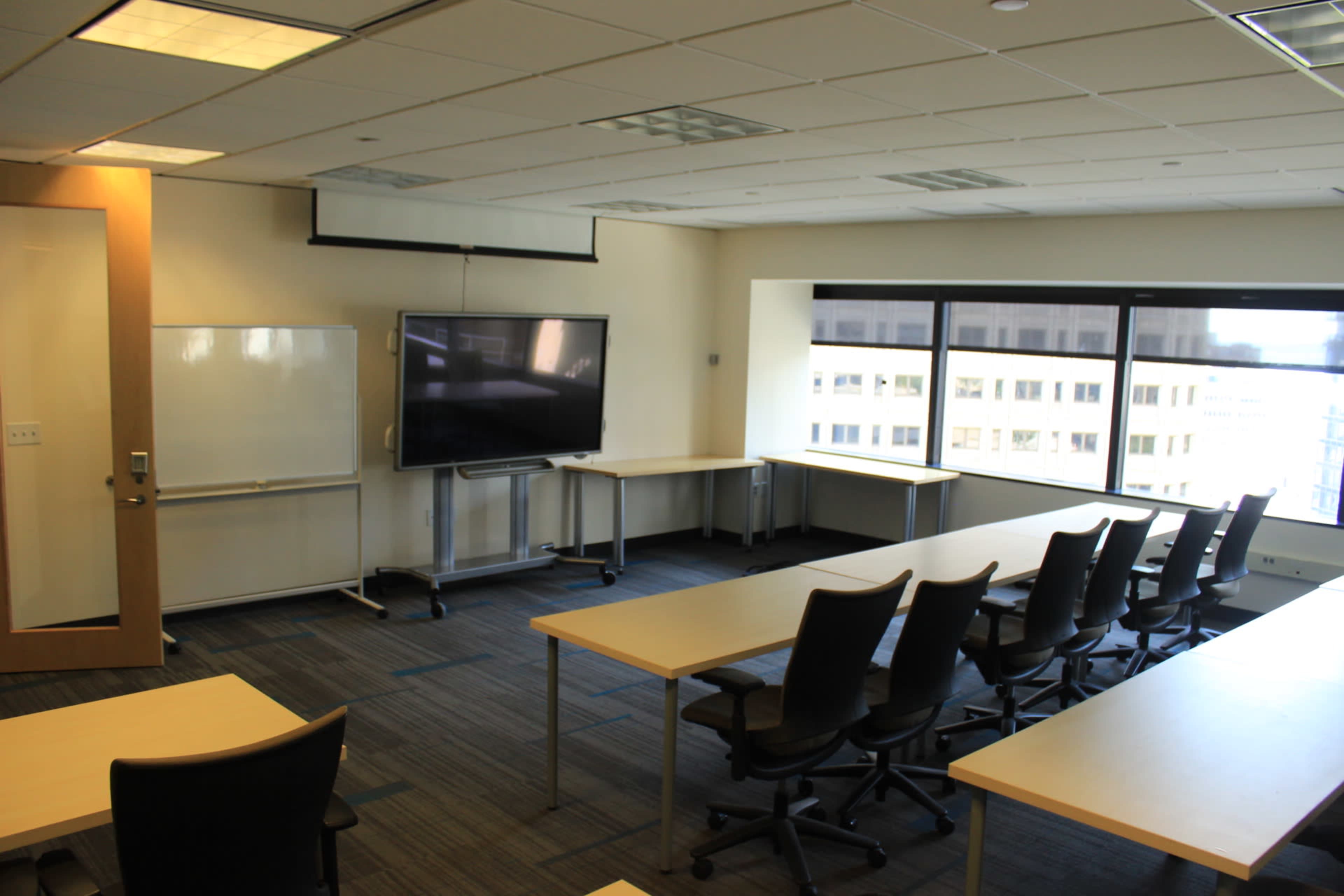 The room features a modern conference setup with a large screen, whiteboard, and several tables surrounded by chairs.