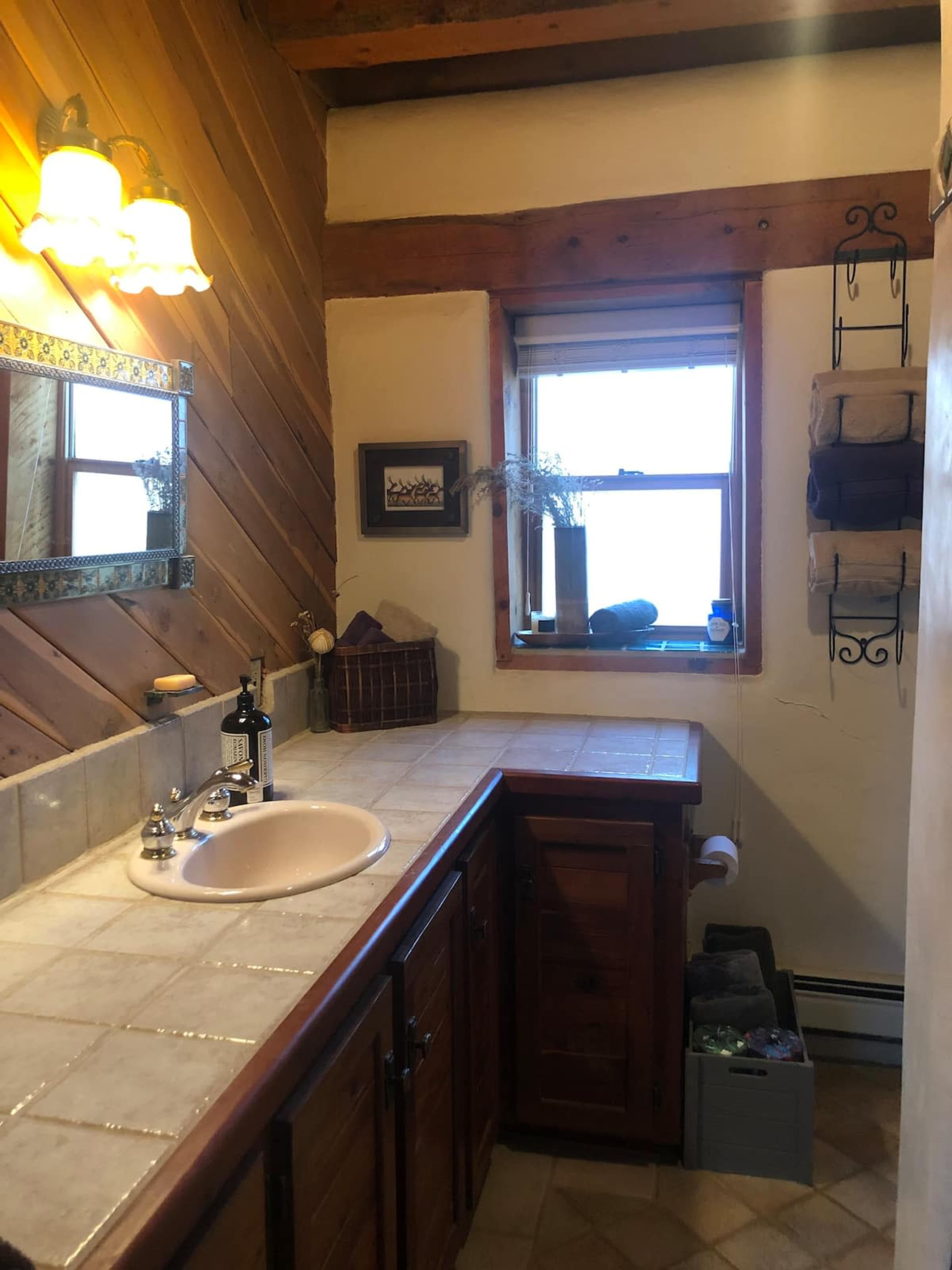A bathroom with a tiled countertop, a sink, wooden cabinets, and a window providing natural light.