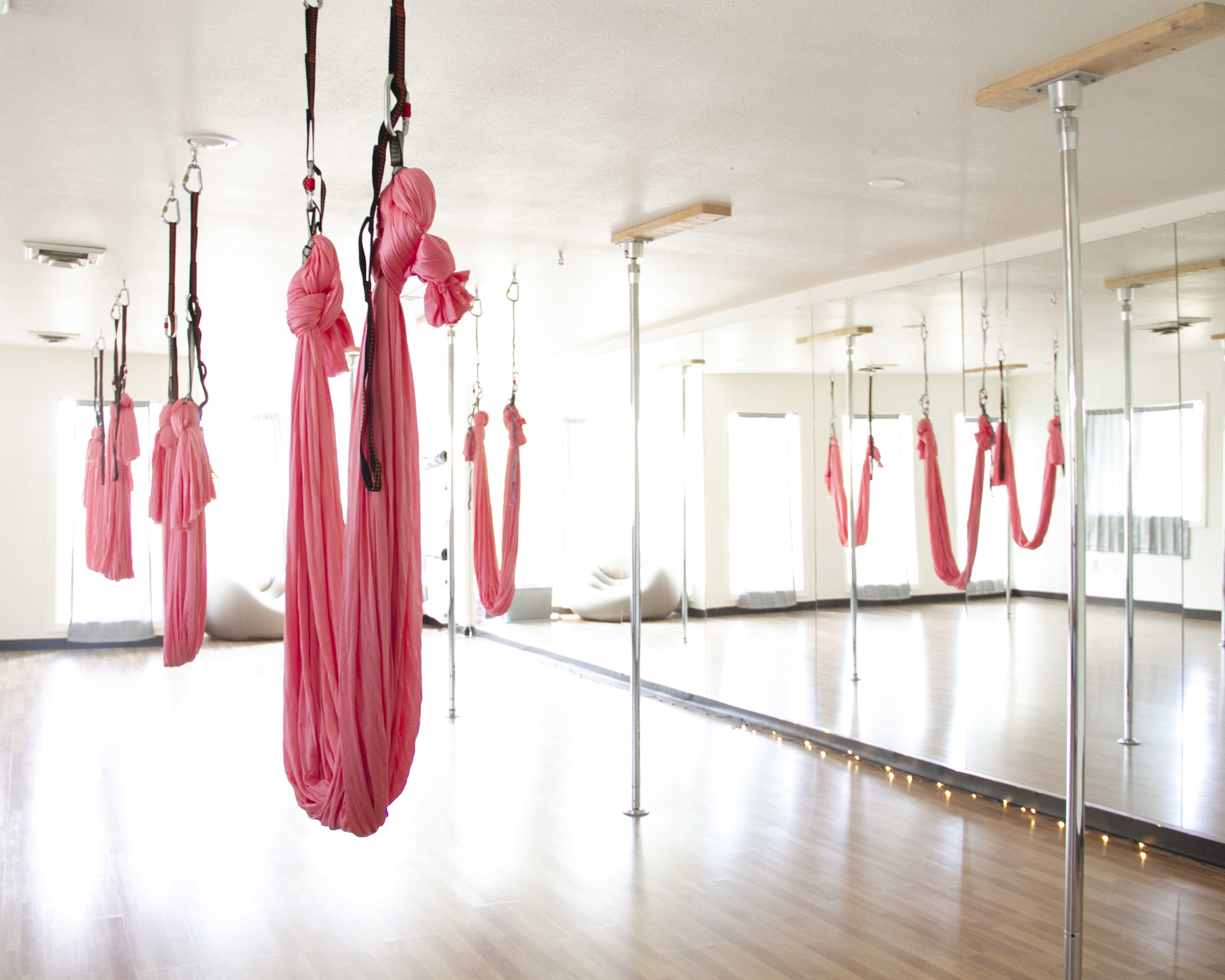 A spacious studio with bright lighting and several pink aerial hammocks suspended from the ceiling.