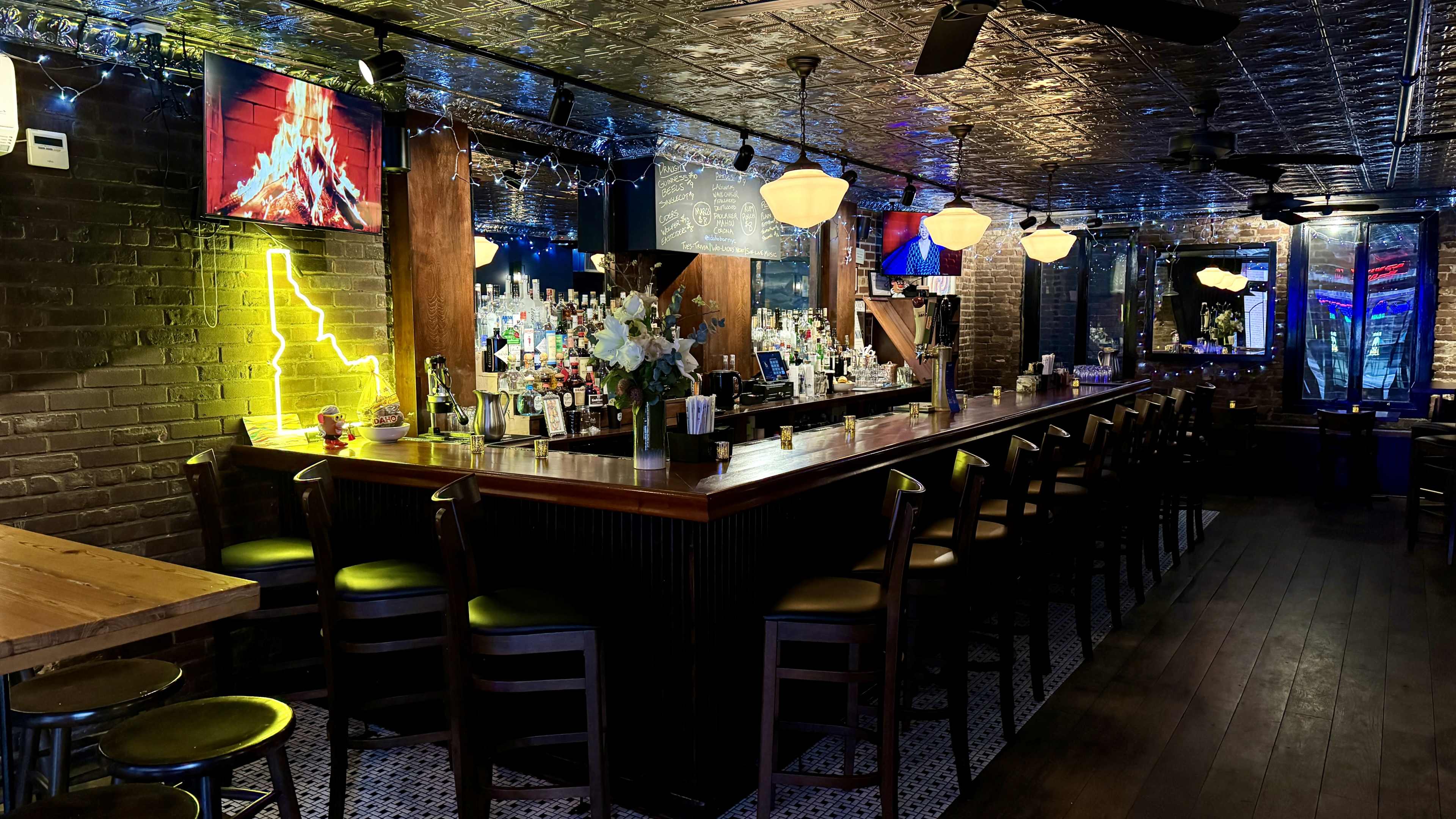 A dimly lit bar area with a long wooden counter, shelves stocked with drinks, and multiple flat-screen TVs mounted on the walls.