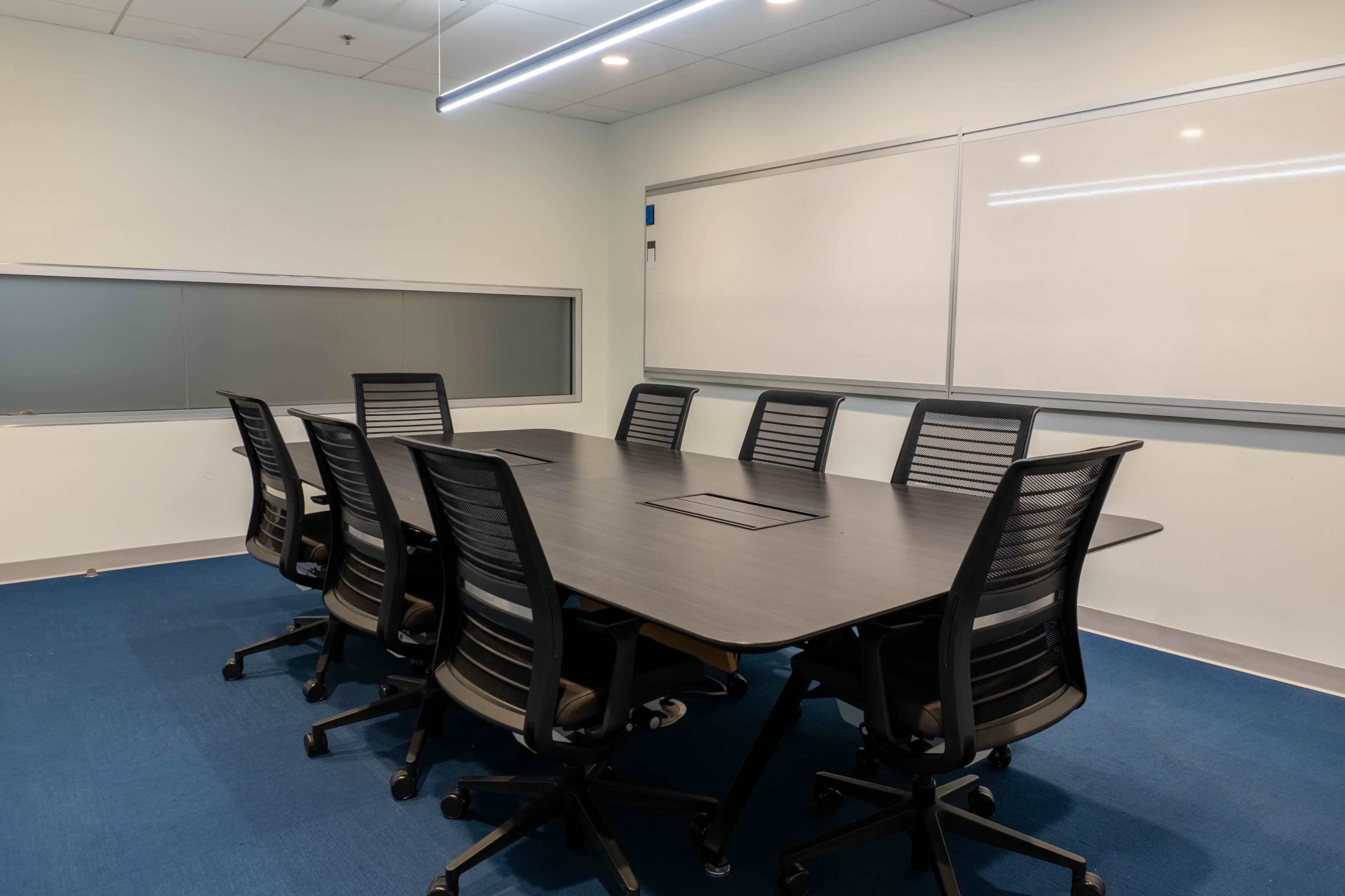 A modern conference room with a long table surrounded by eight black ergonomic chairs and a whiteboard on the wall.