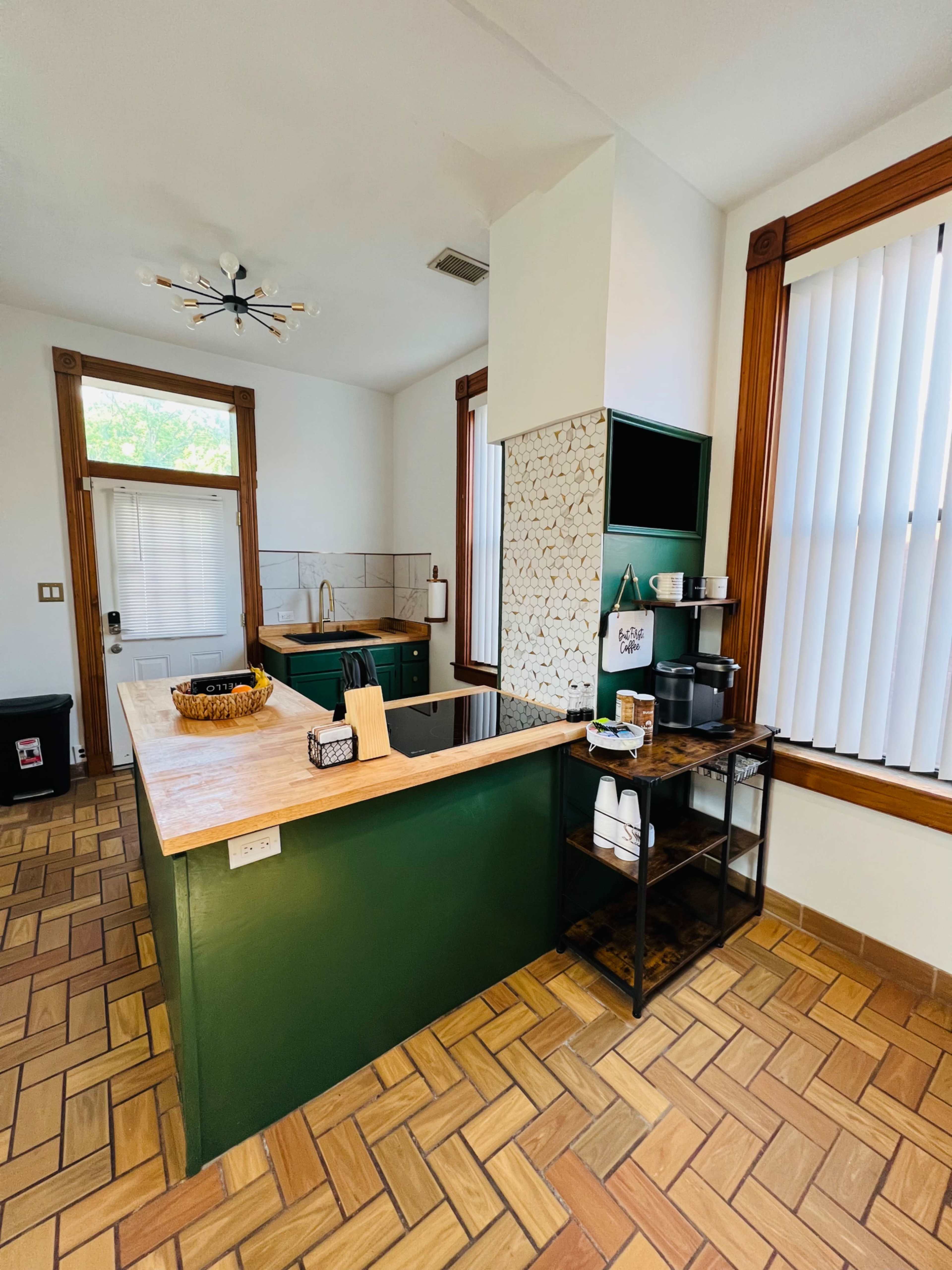 A modern kitchen featuring green cabinets, a wooden countertop, and a tiled backsplash, with large windows allowing natural light to enter.