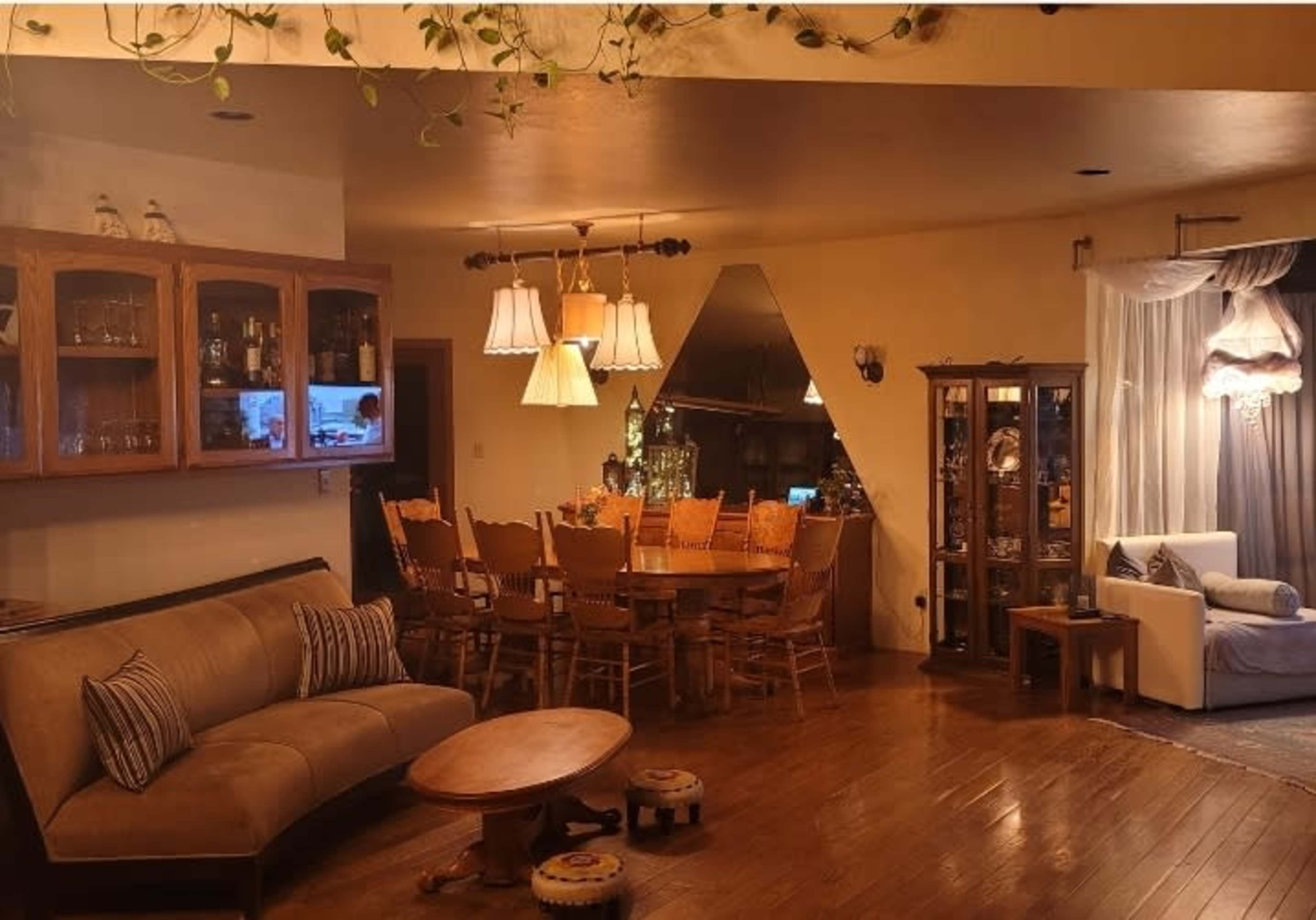 A cozy dining and living area with a wooden dining table surrounded by chairs, a couch, and glass display cabinets.
