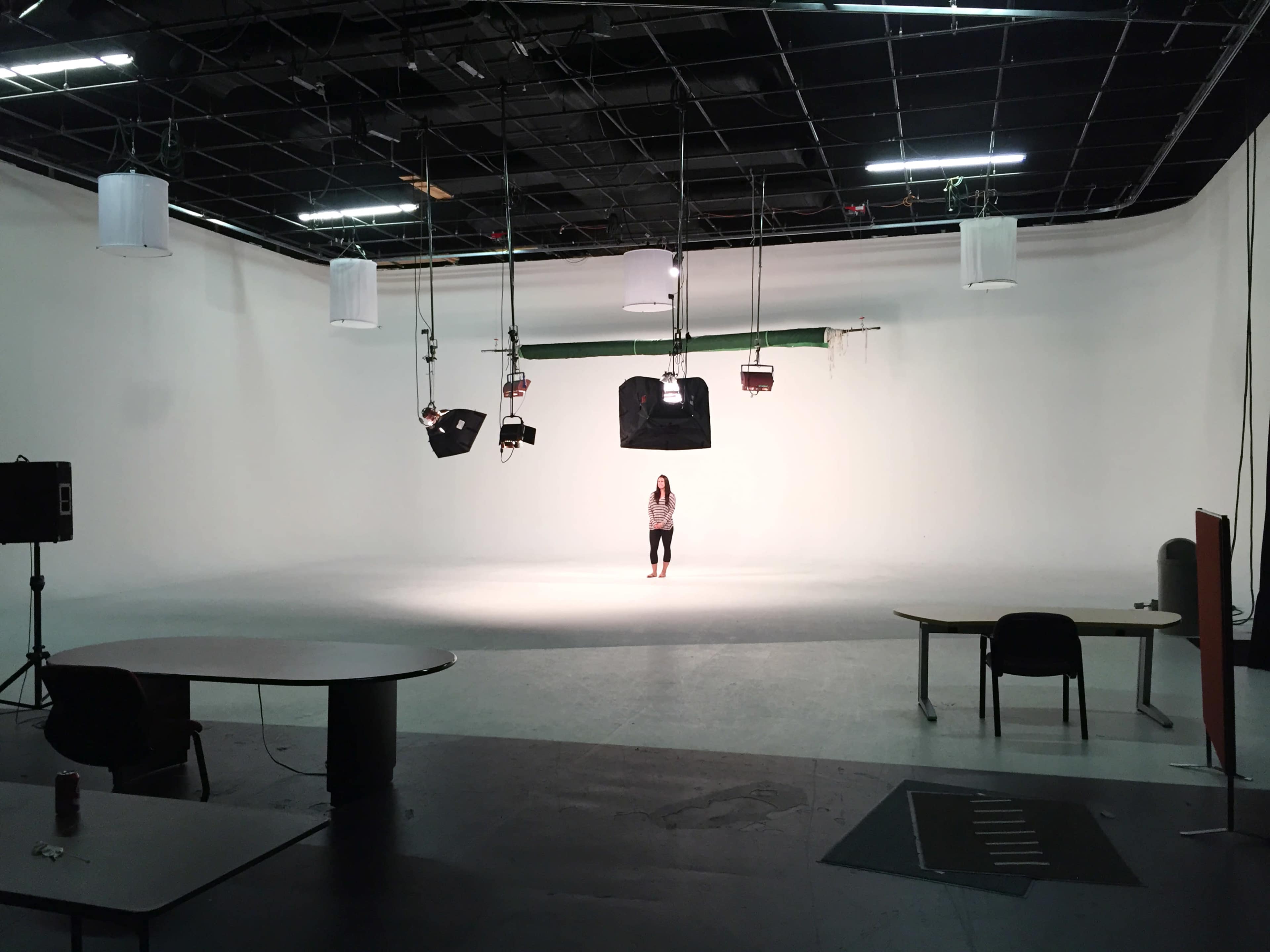 A person stands alone in a spacious, empty studio with a white backdrop and lighting equipment overhead.