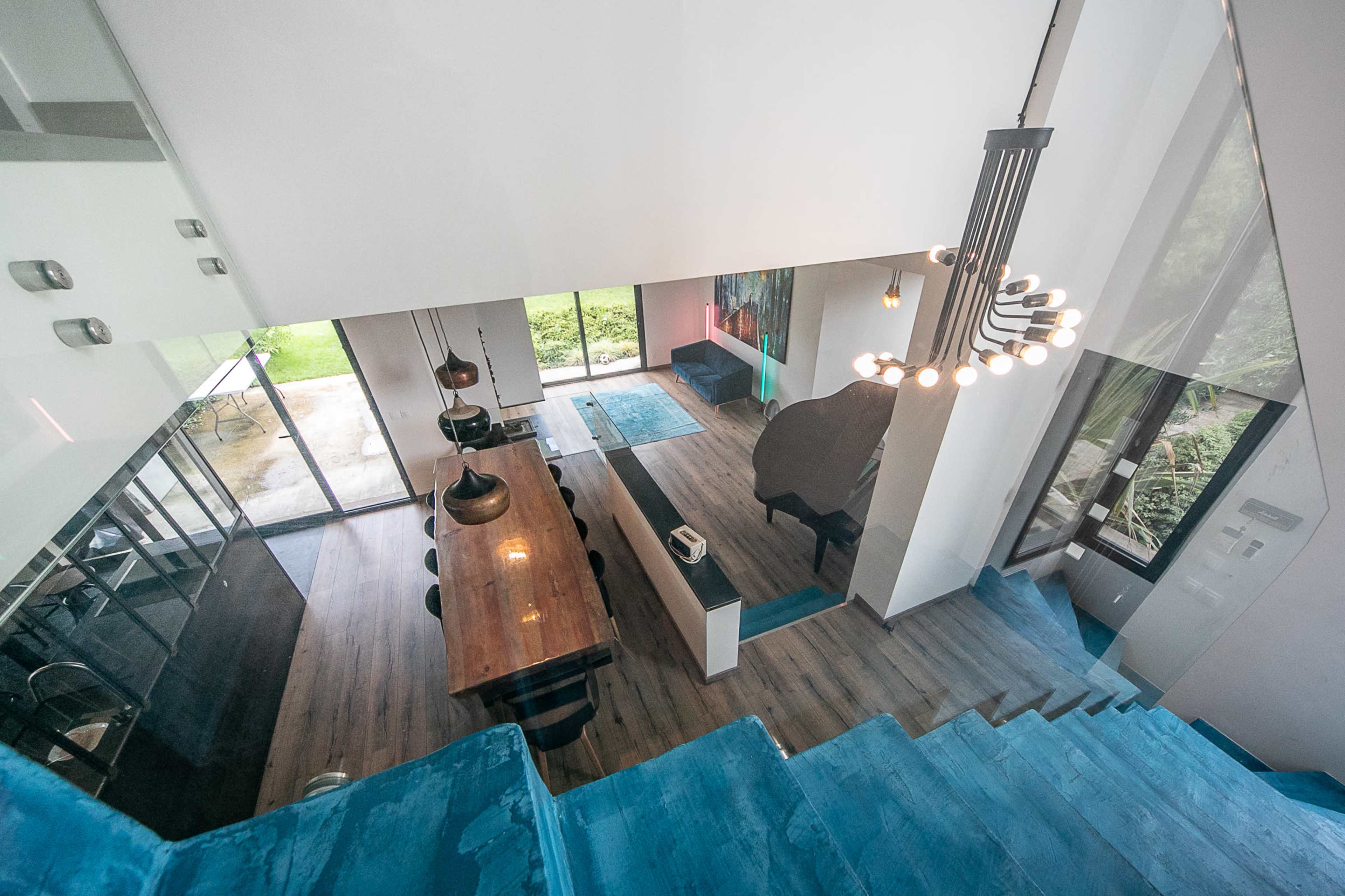 A modern, open-concept home interior with a wooden dining table, black pendant lights, and large glass doors leading to an outdoor area.