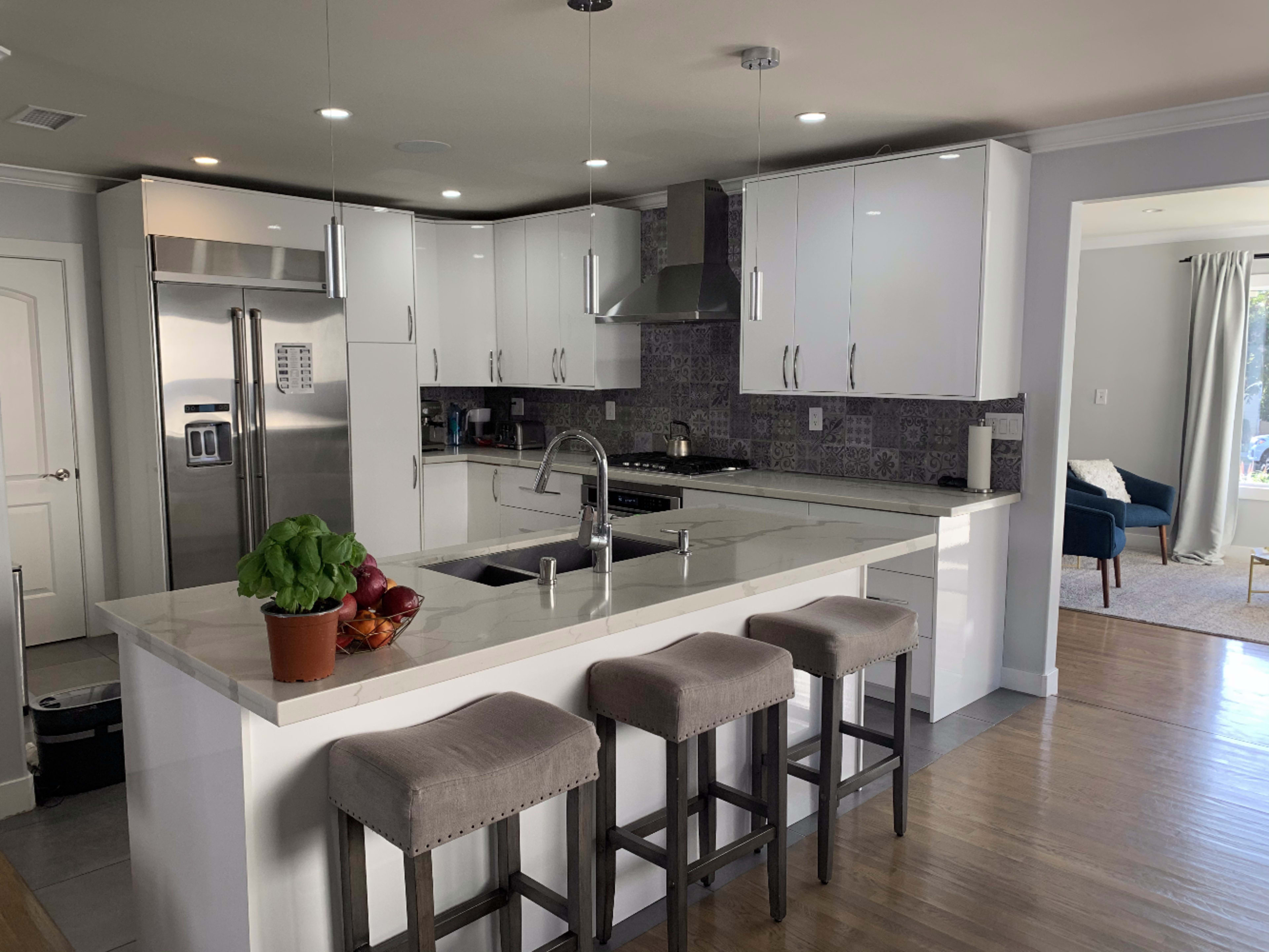The image depicts a modern kitchen featuring a white countertop, stainless steel appliances, and bar stools along a kitchen island.