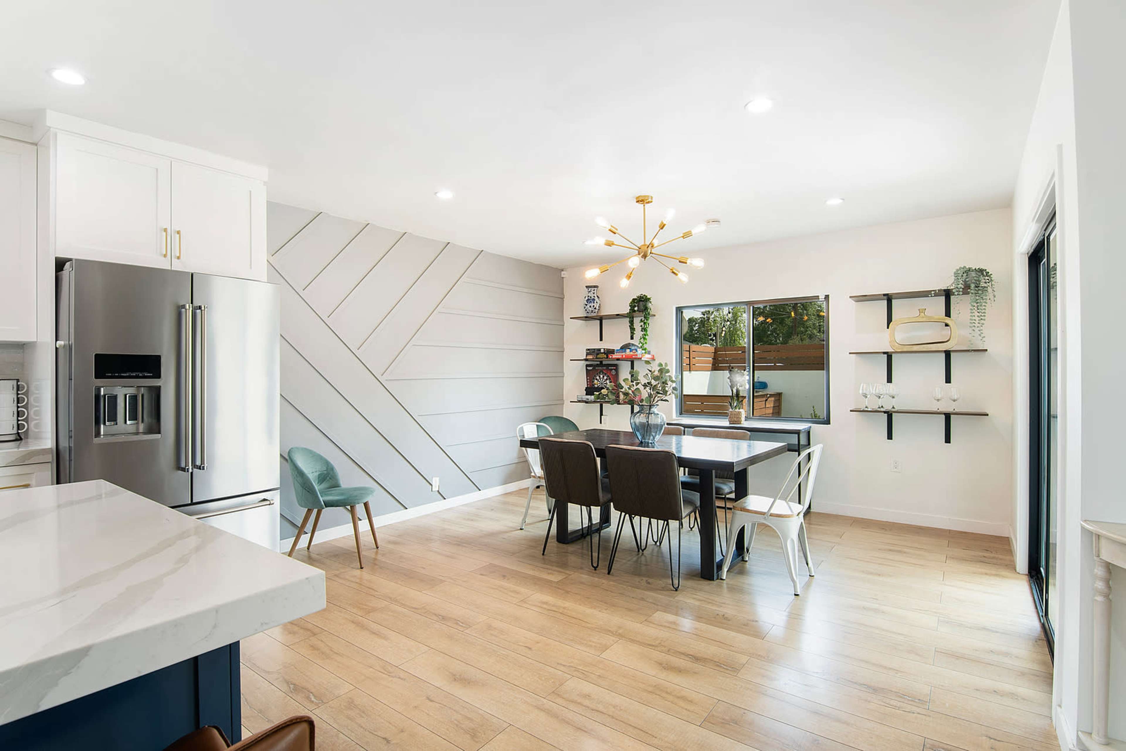 The image shows a modern kitchen-dining area featuring a large table, sleek cabinets, and a decorative accent wall.