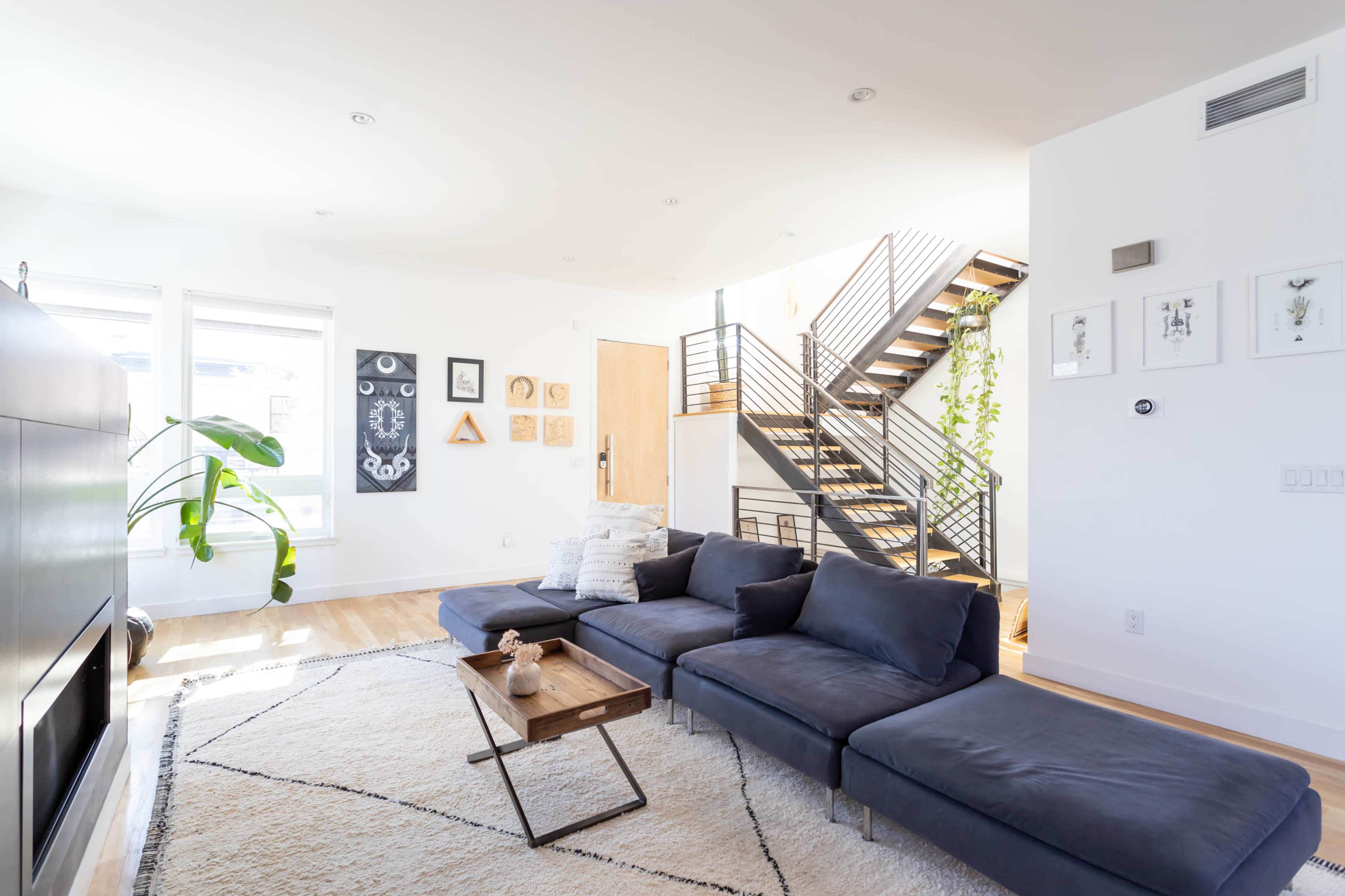 A modern living room with a dark sectional sofa, a wooden coffee table, and decorative wall art, adjacent to a staircase with metal railings.