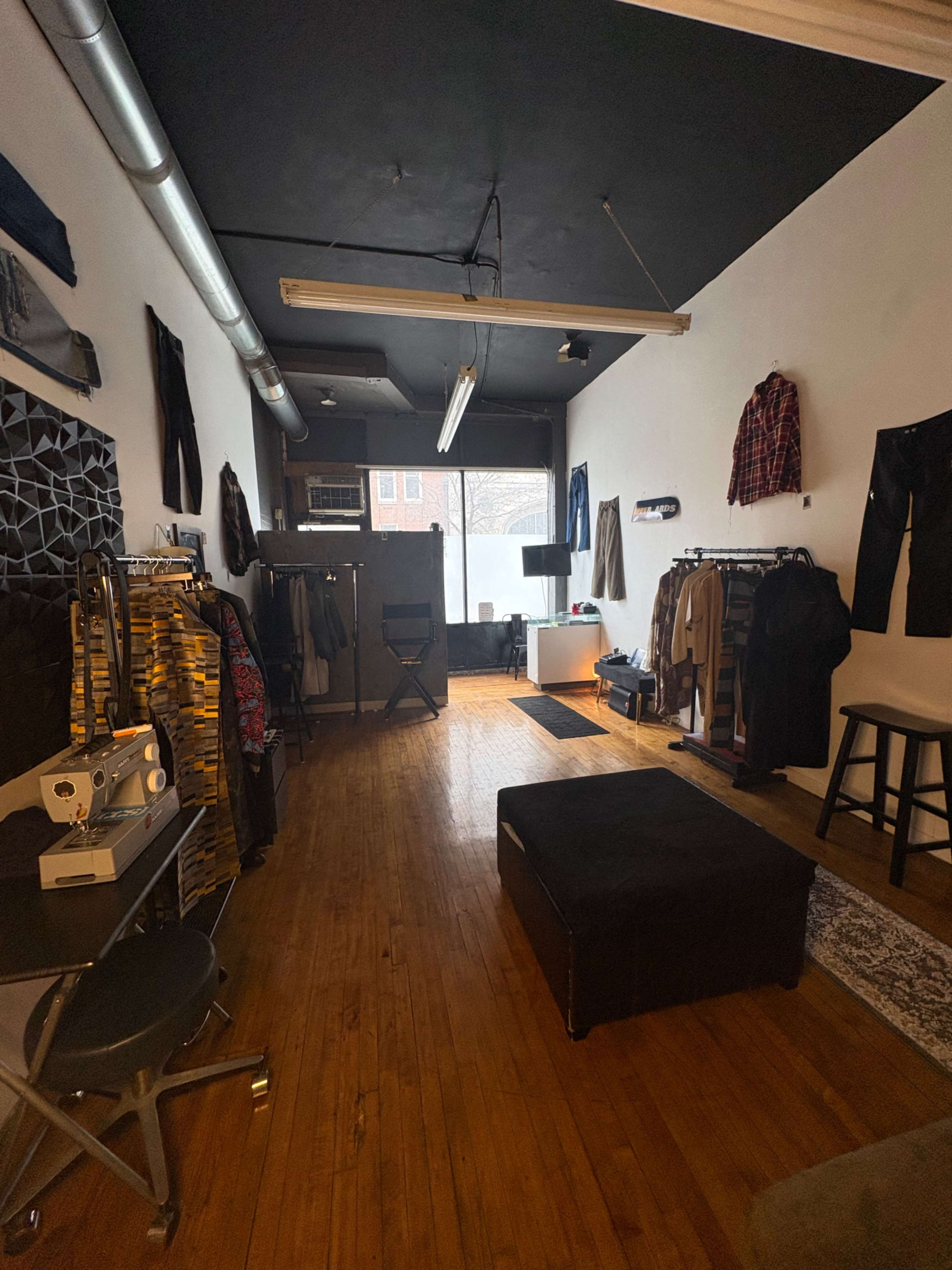 The image shows a clothing boutique with racks of garments along the walls, a sewing machine on a table, and natural light coming through a large window.