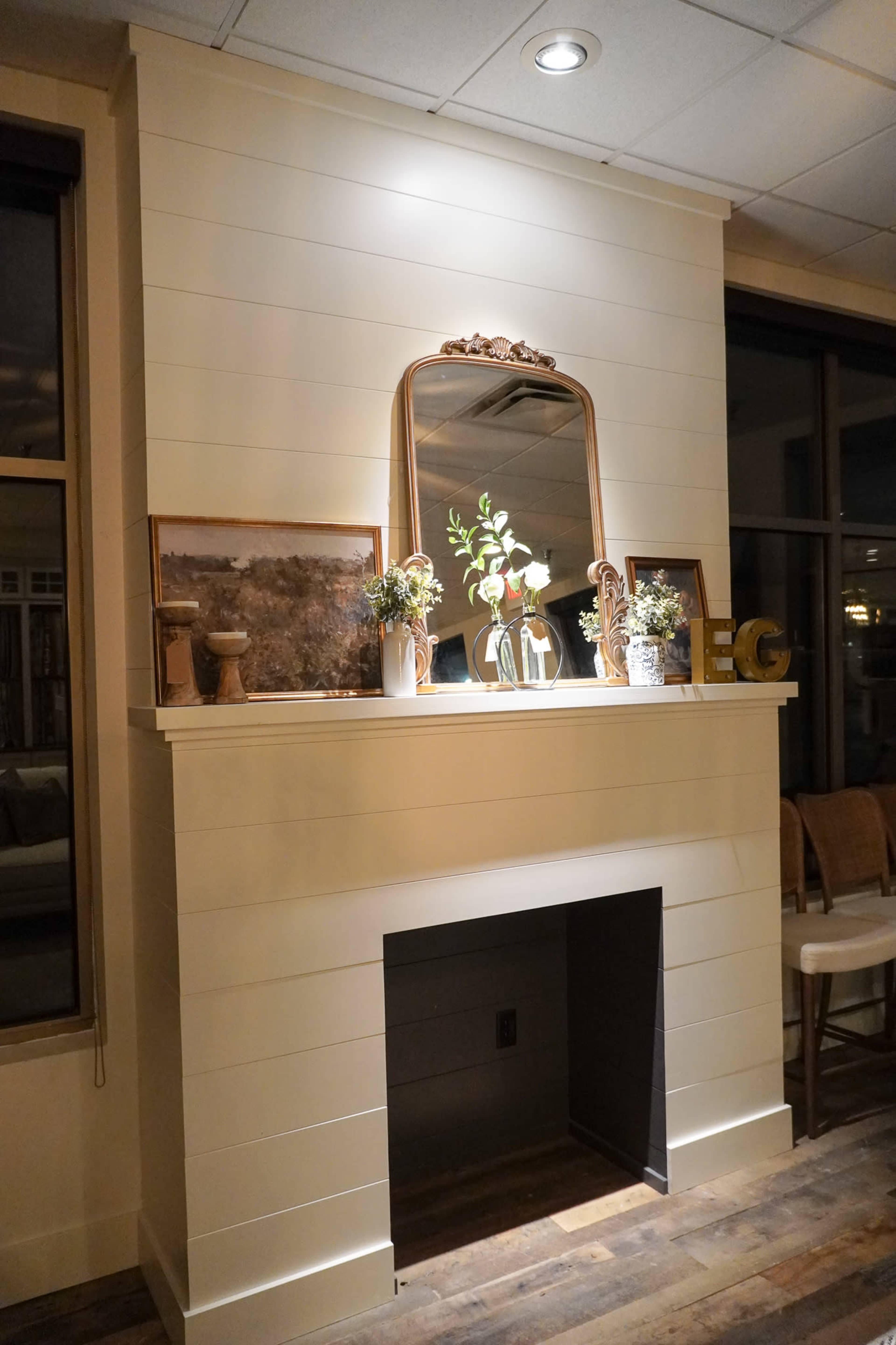 A modern living room with a white shiplap fireplace, a decorative mirror, and several framed pictures arranged on the mantel.