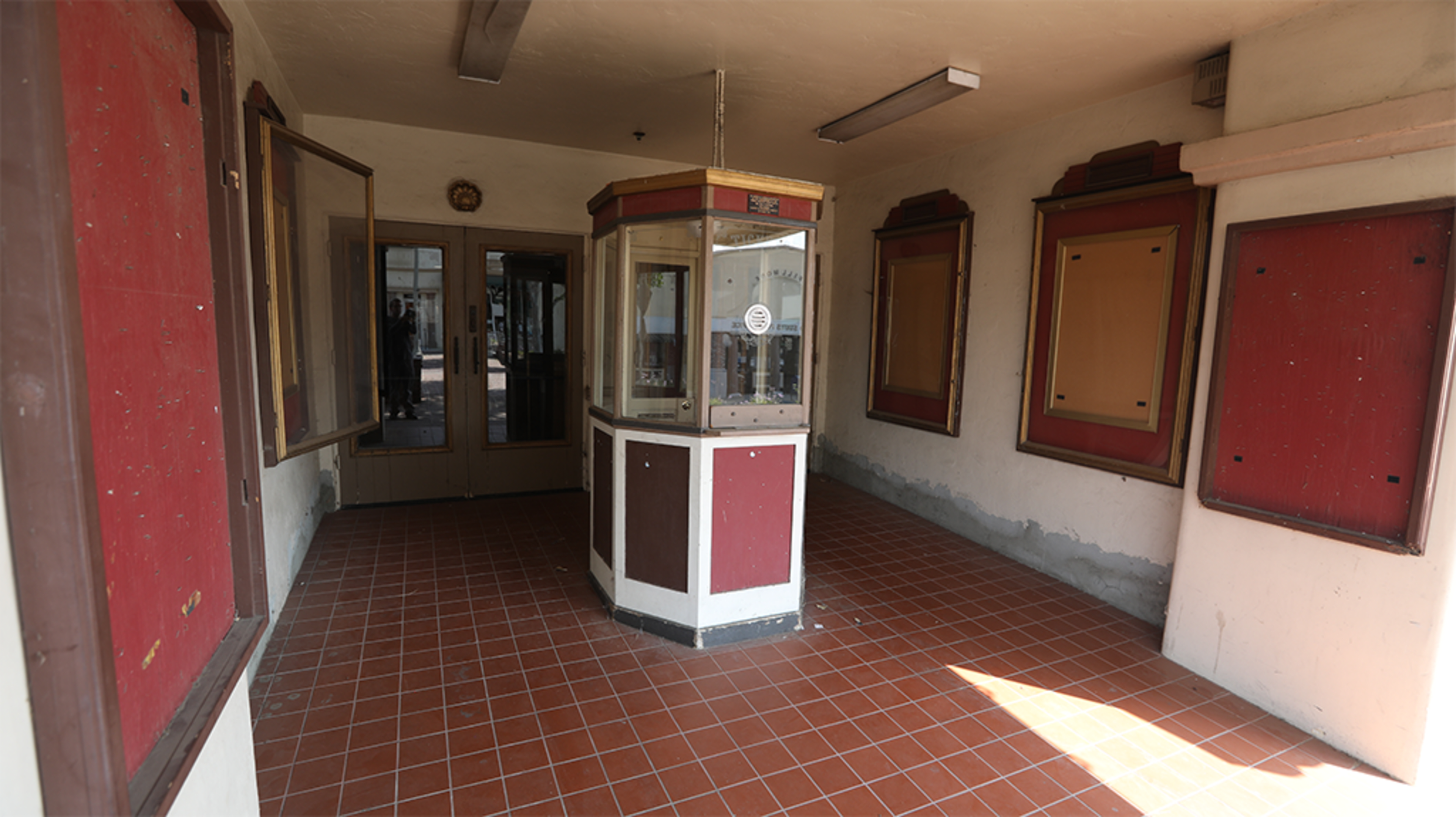An empty ticket booth area with red and white walls, tiled flooring, and vacant display boards.