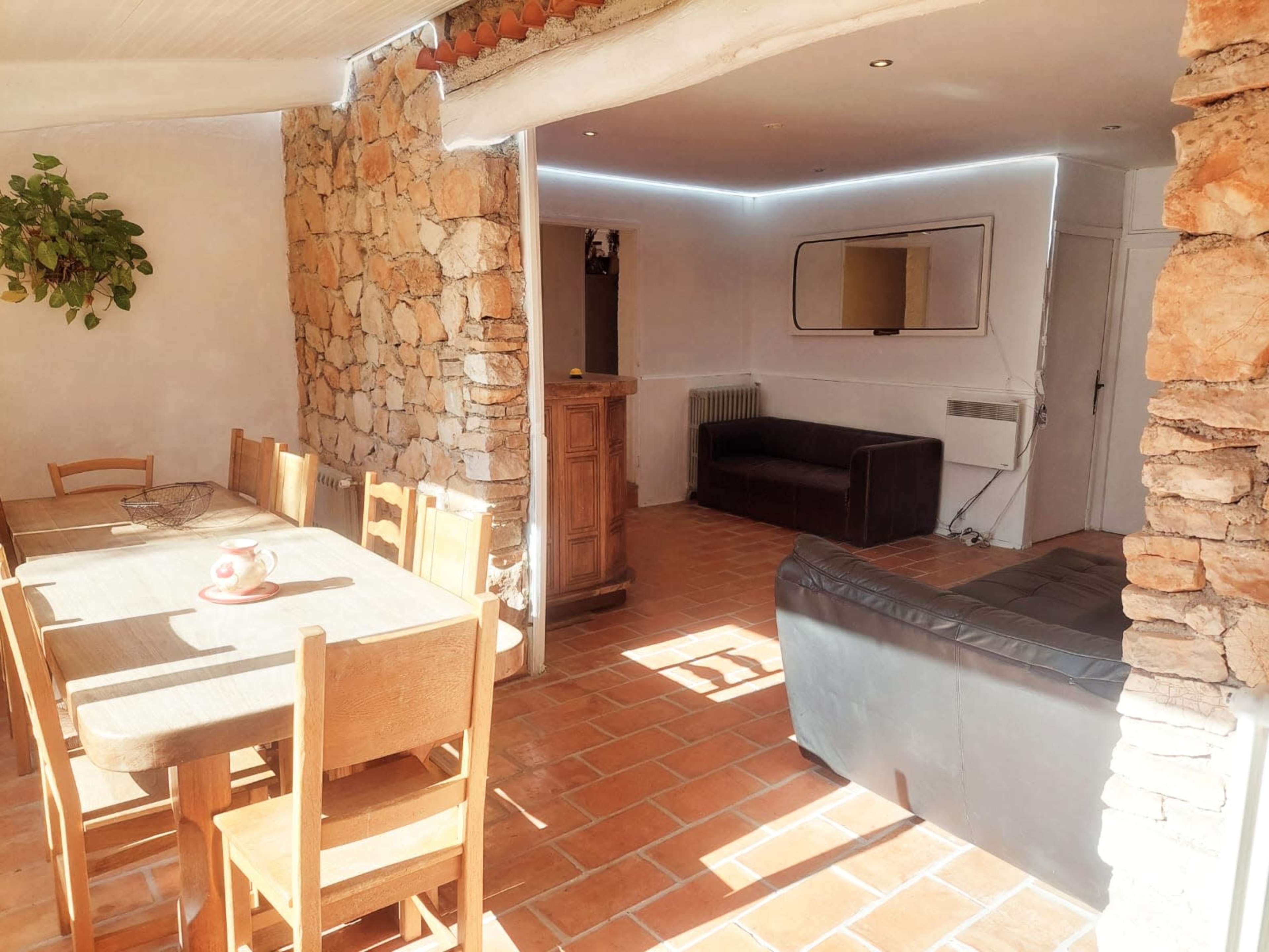 The image shows a rustic interior with a stone wall, wooden dining table and chairs, a dark couch, and subtle LED lighting.