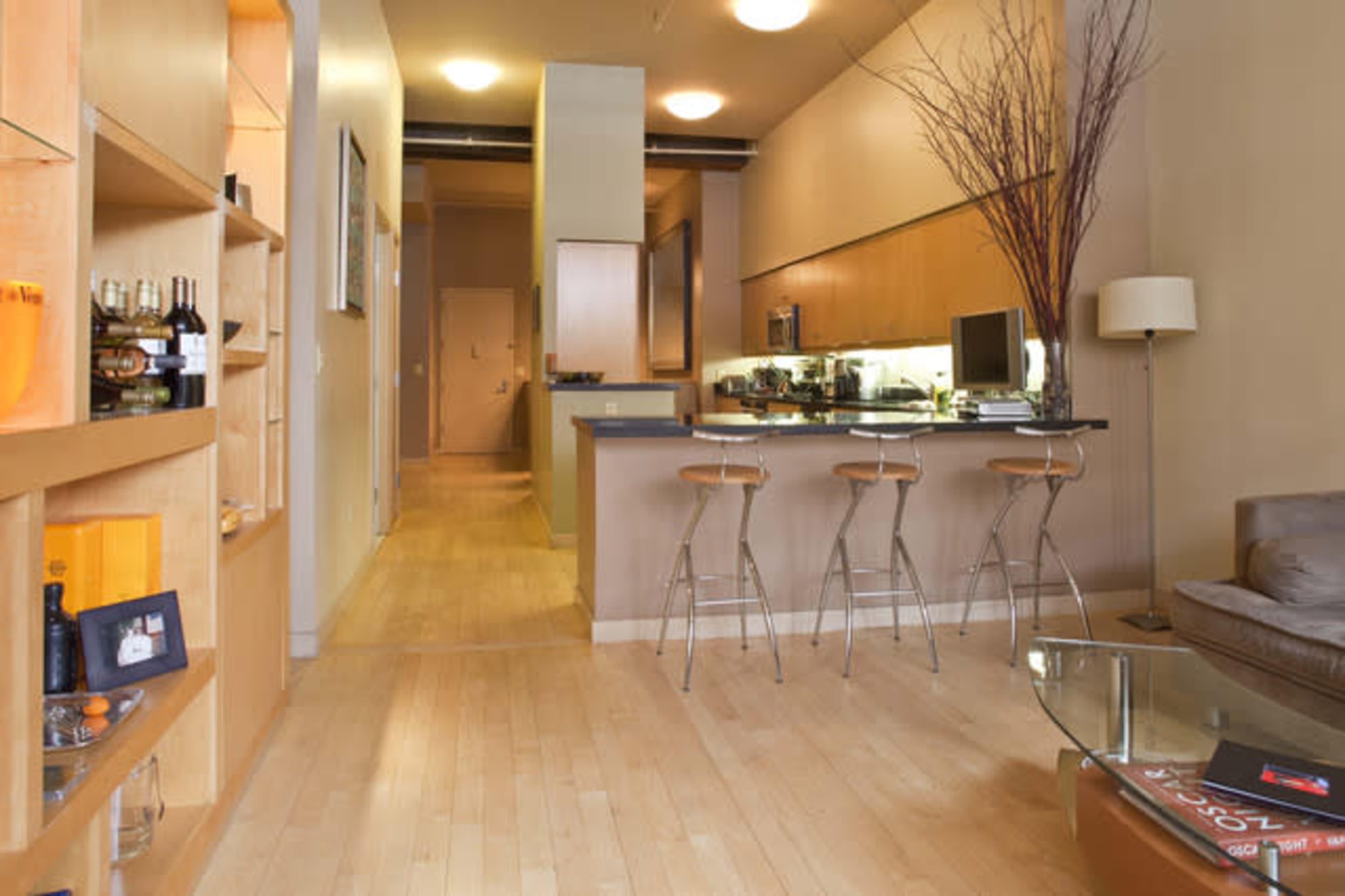 A modern apartment interior featuring a kitchen area with bar stools, hardwood floors, and a living space with a sofa and decorative items.