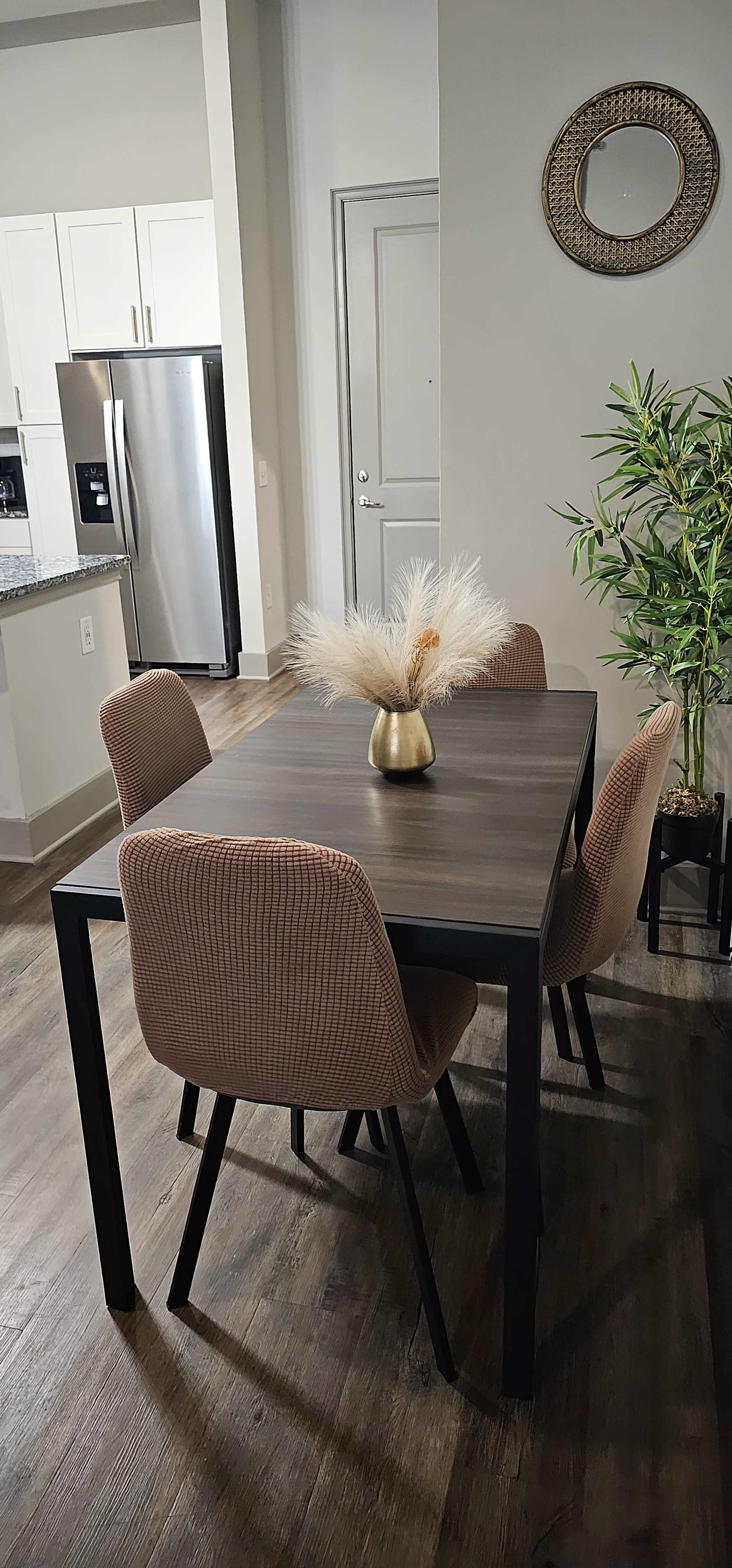 A modern dining area features a wooden table with four upholstered chairs and a decorative vase with dried plants.