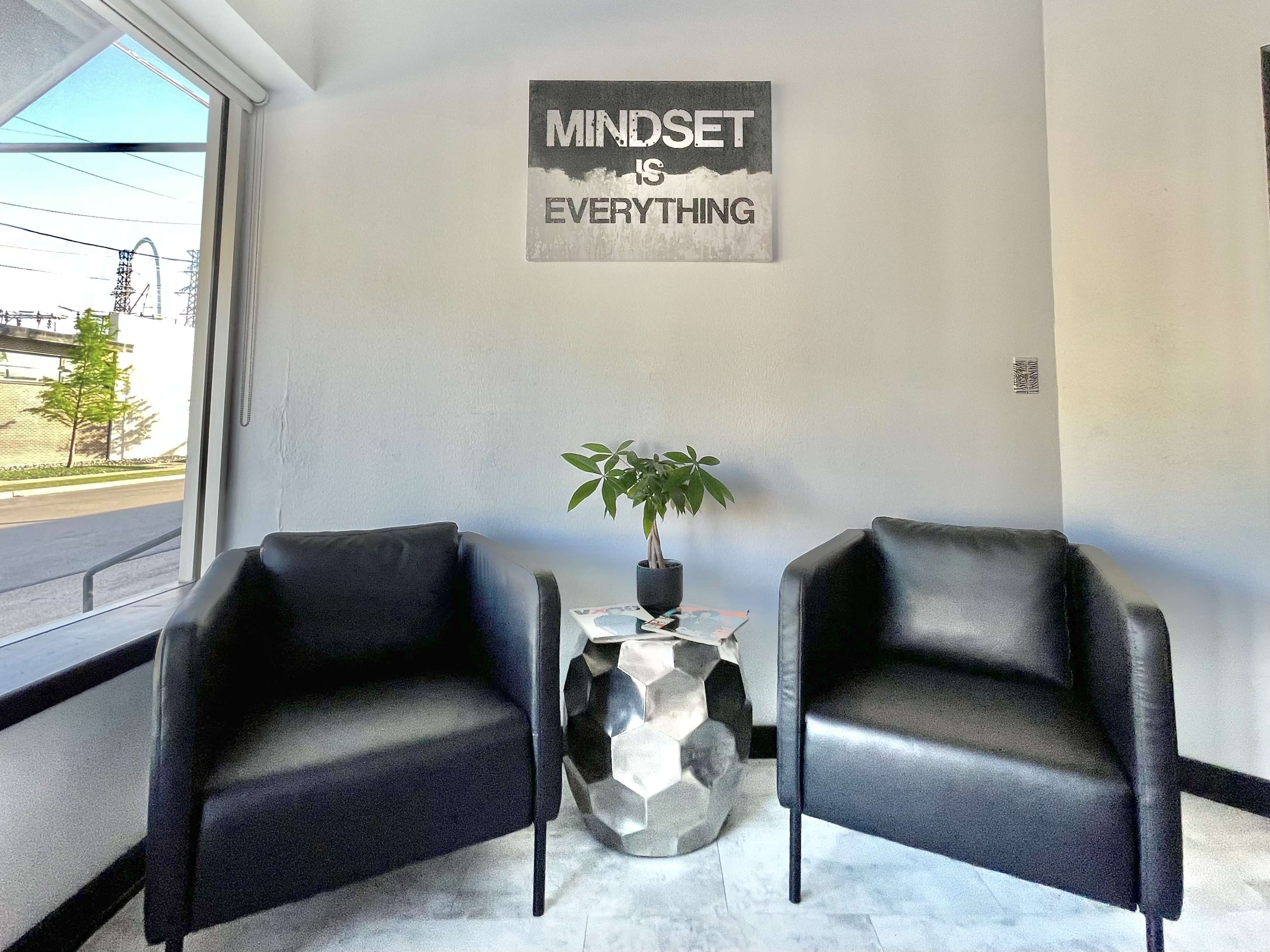 A corner seating area with two black armchairs, a geometric side table, and a potted plant under a motivational sign that reads "MINDSET IS EVERYTHING."