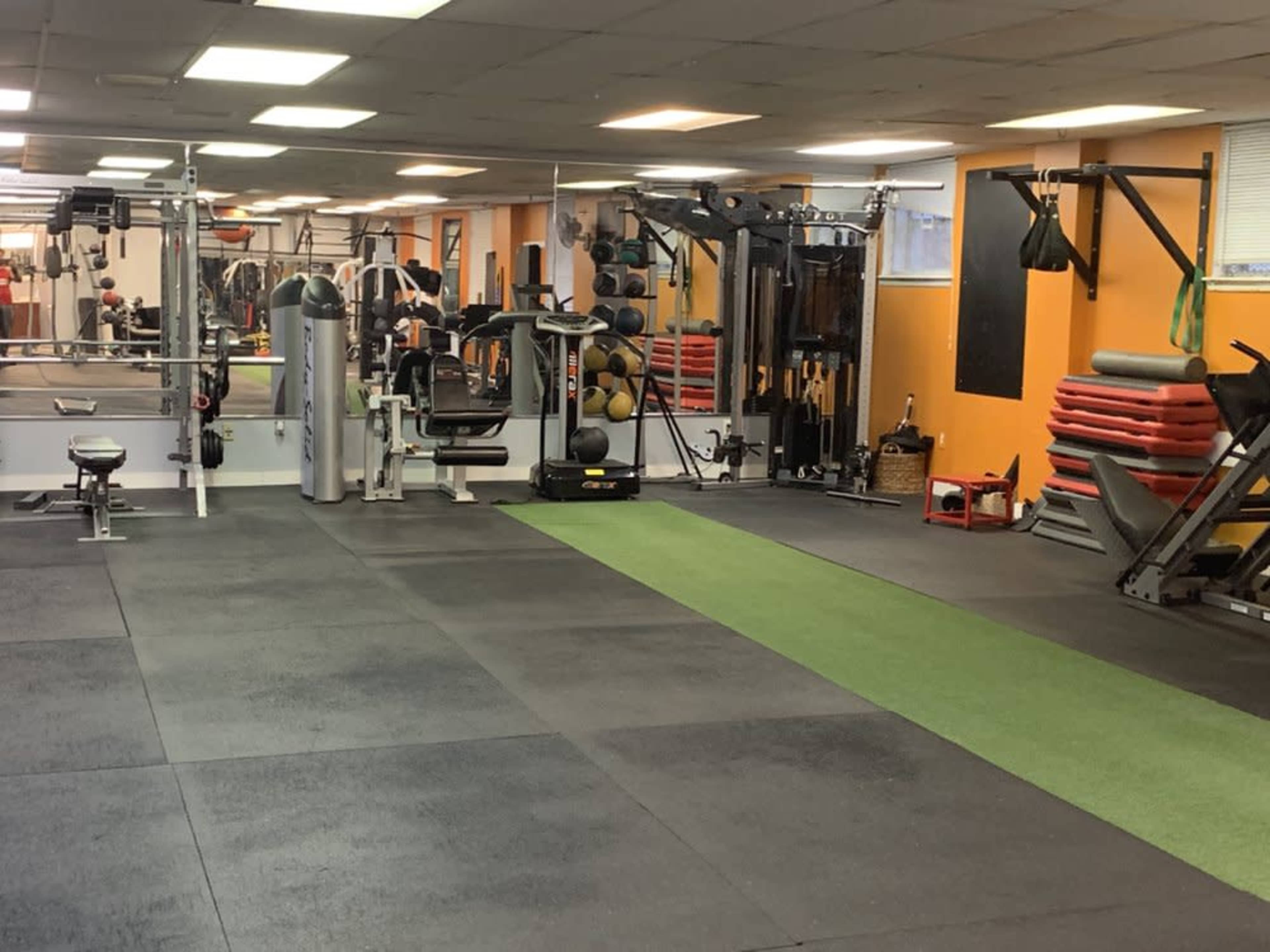 A spacious gym floor with various exercise equipment, including weight machines, free weights, and a green turf area.
