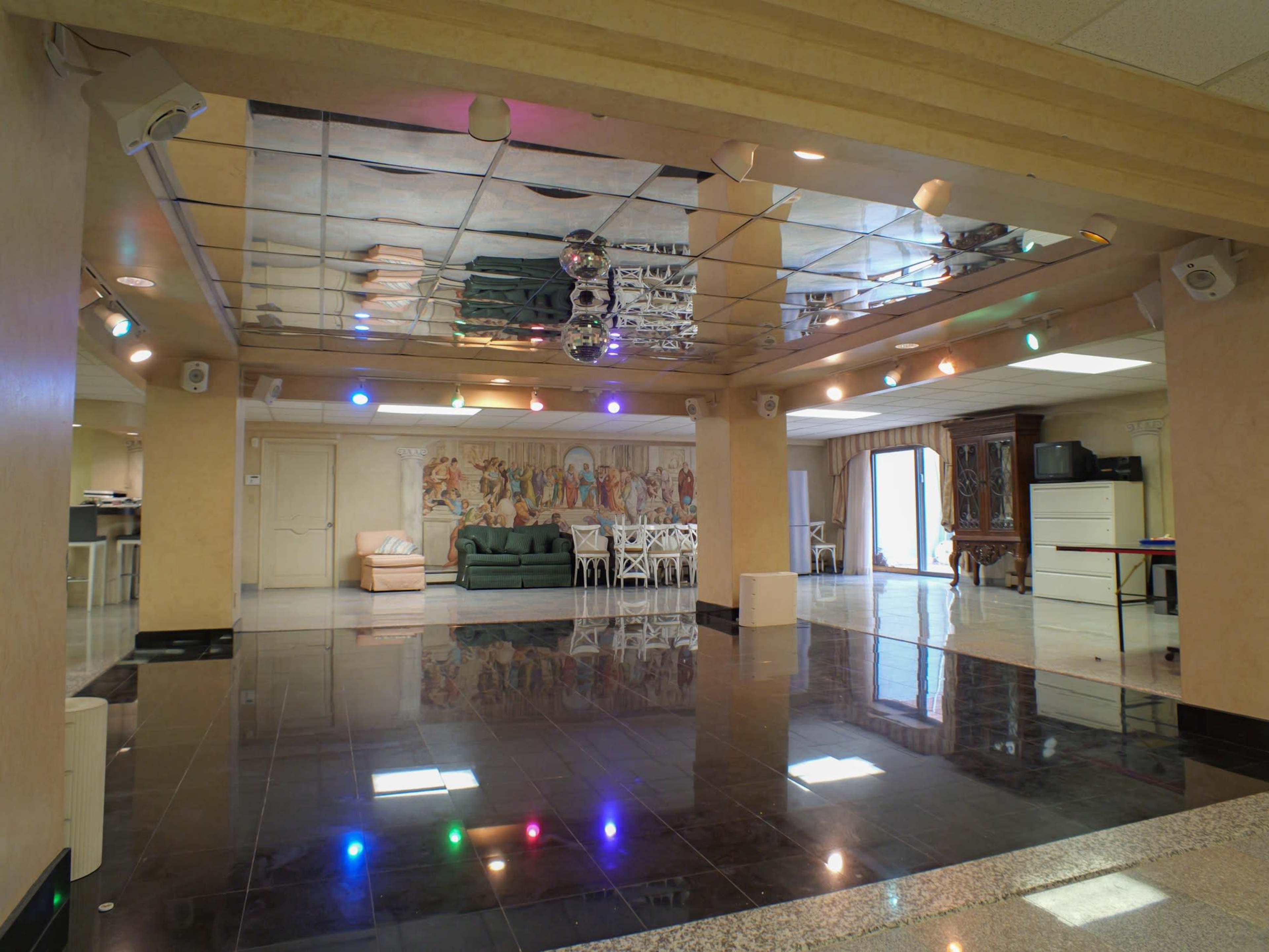 The image shows a spacious interior with a mirrored ceiling, black tiled floor, and a green sofa along one wall, illuminated by multicolored lights.