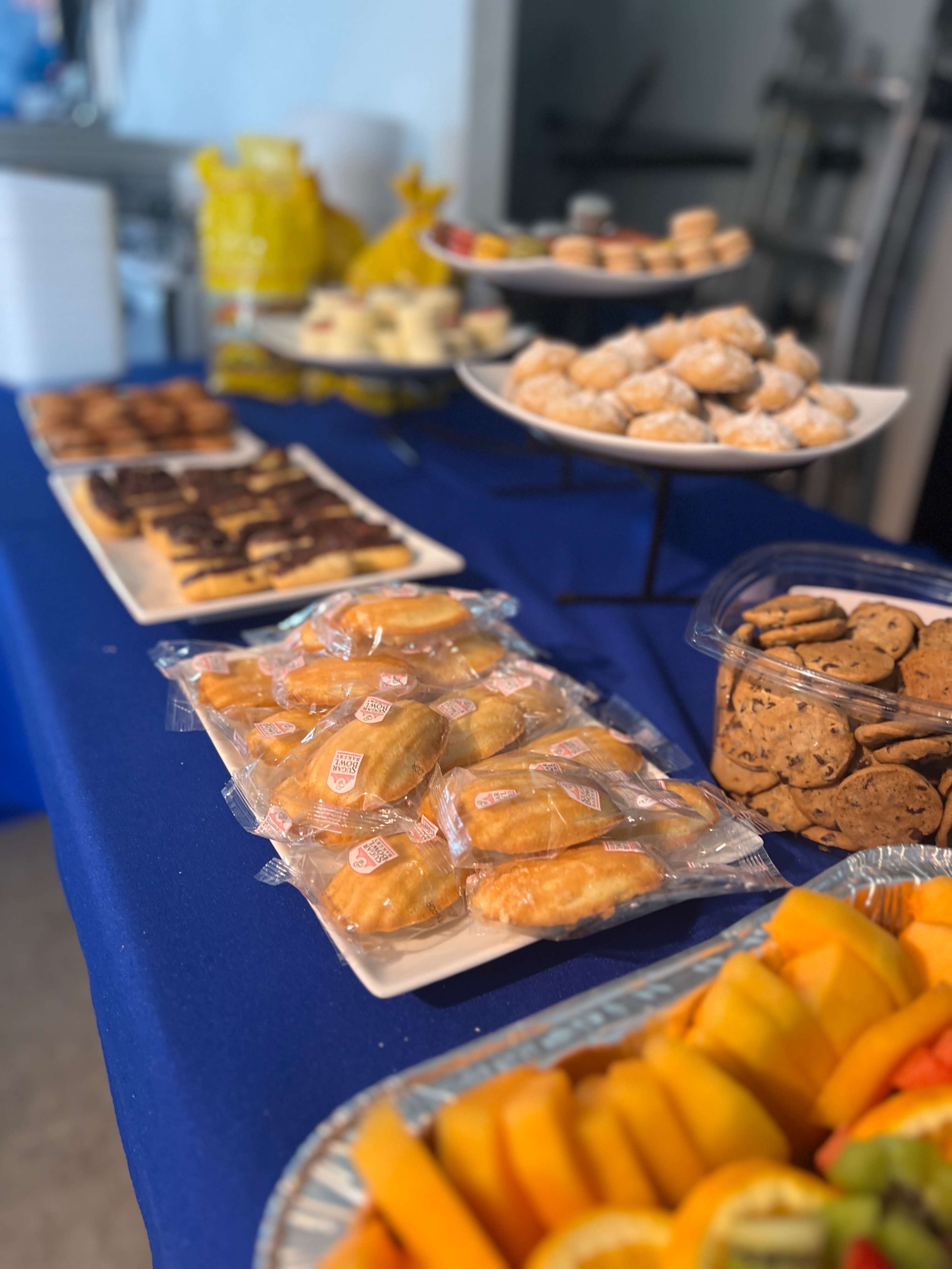 A table is set with various desserts, including cookies, pastries, and fruit slices, arranged on plates and trays.